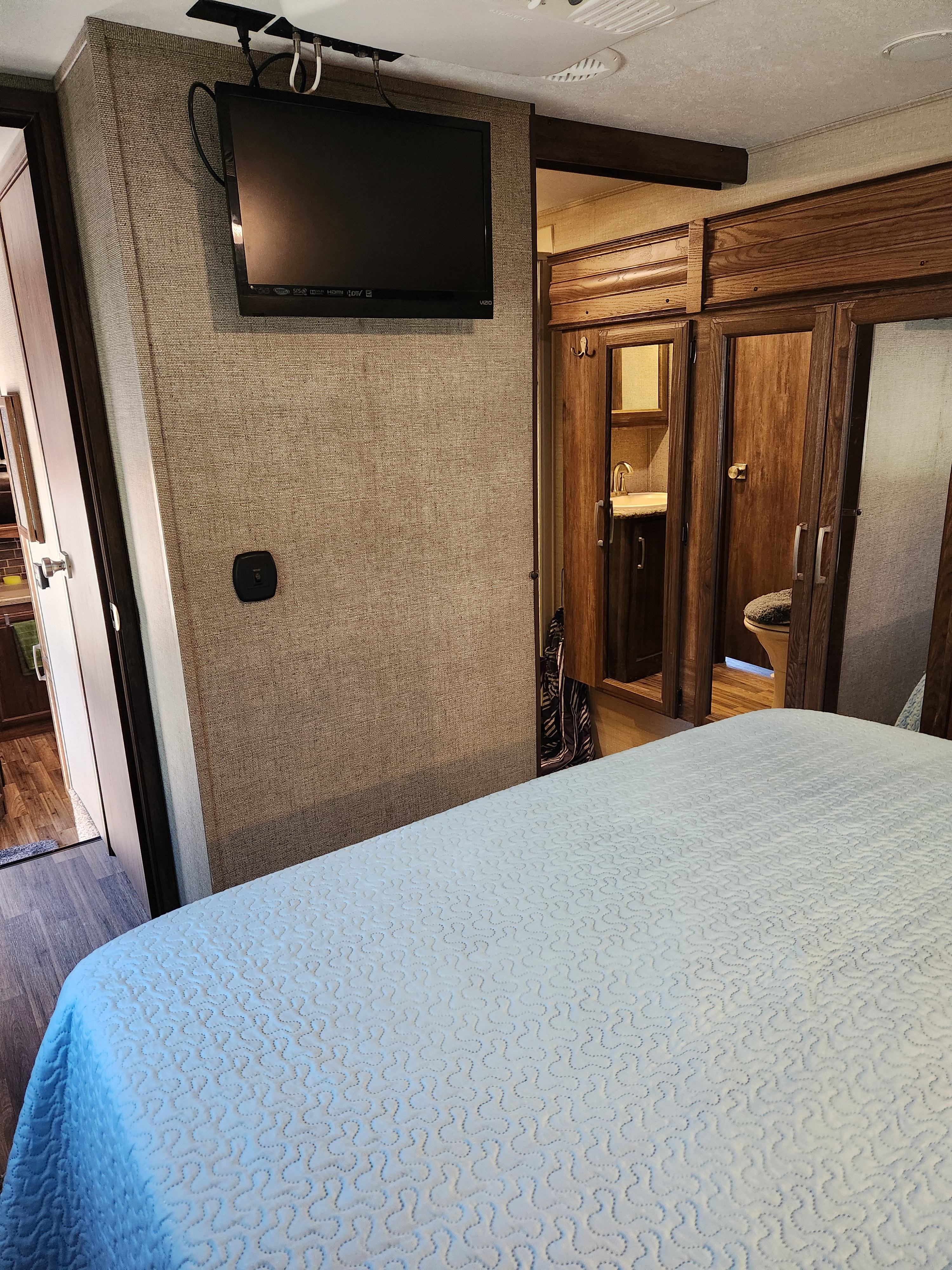 Interior of an RV rental bedroom showing a light blue bed, mounted TV, and an adjacent compact bathroom. Efficient design.. Keystone RV Cougar 2017