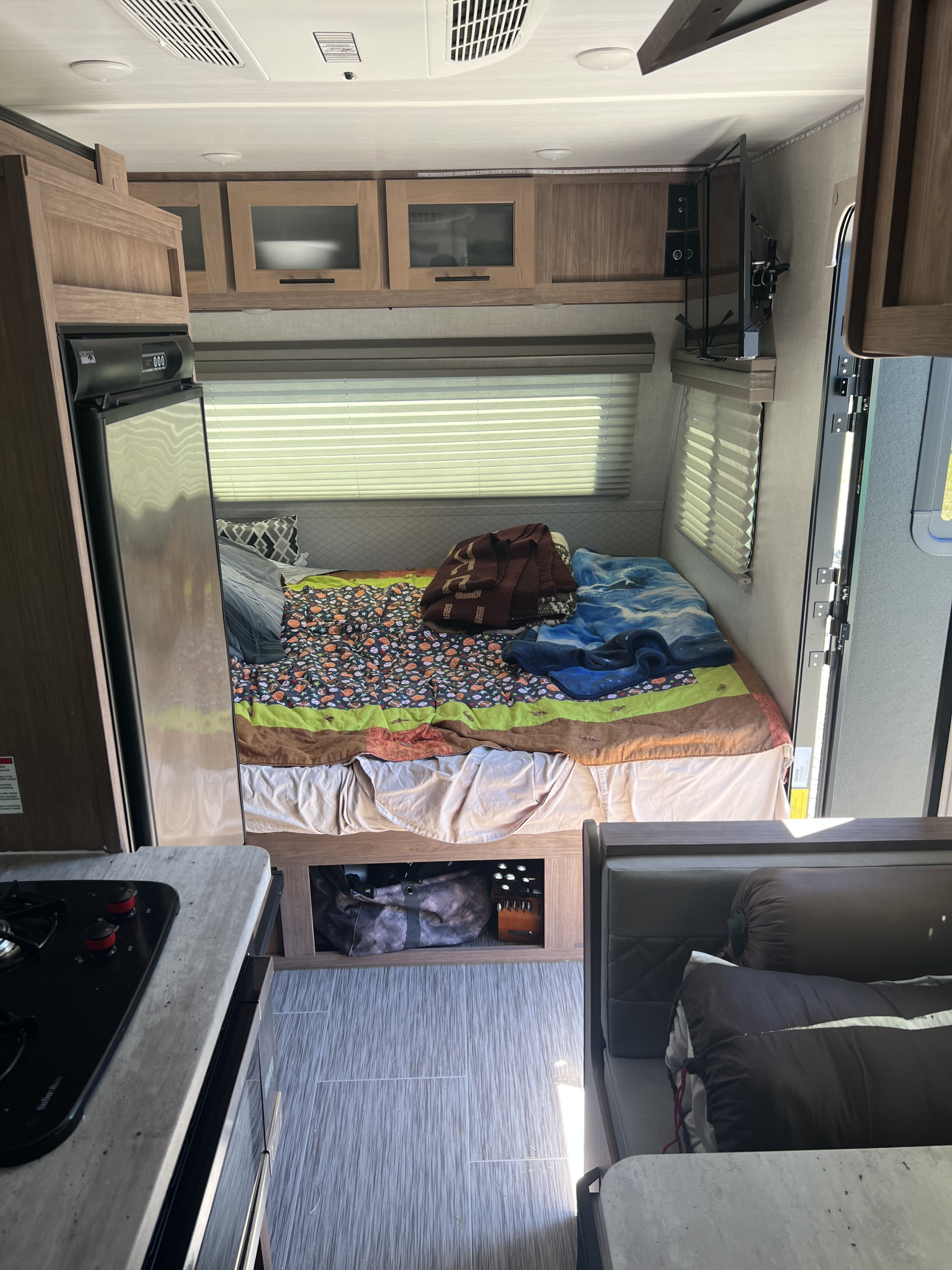 Comfortable RV rental interior with a bed, colorful bedding, mini-fridge, and overhead cabinets, a cozy travel space.. No Boundaries 16 2022