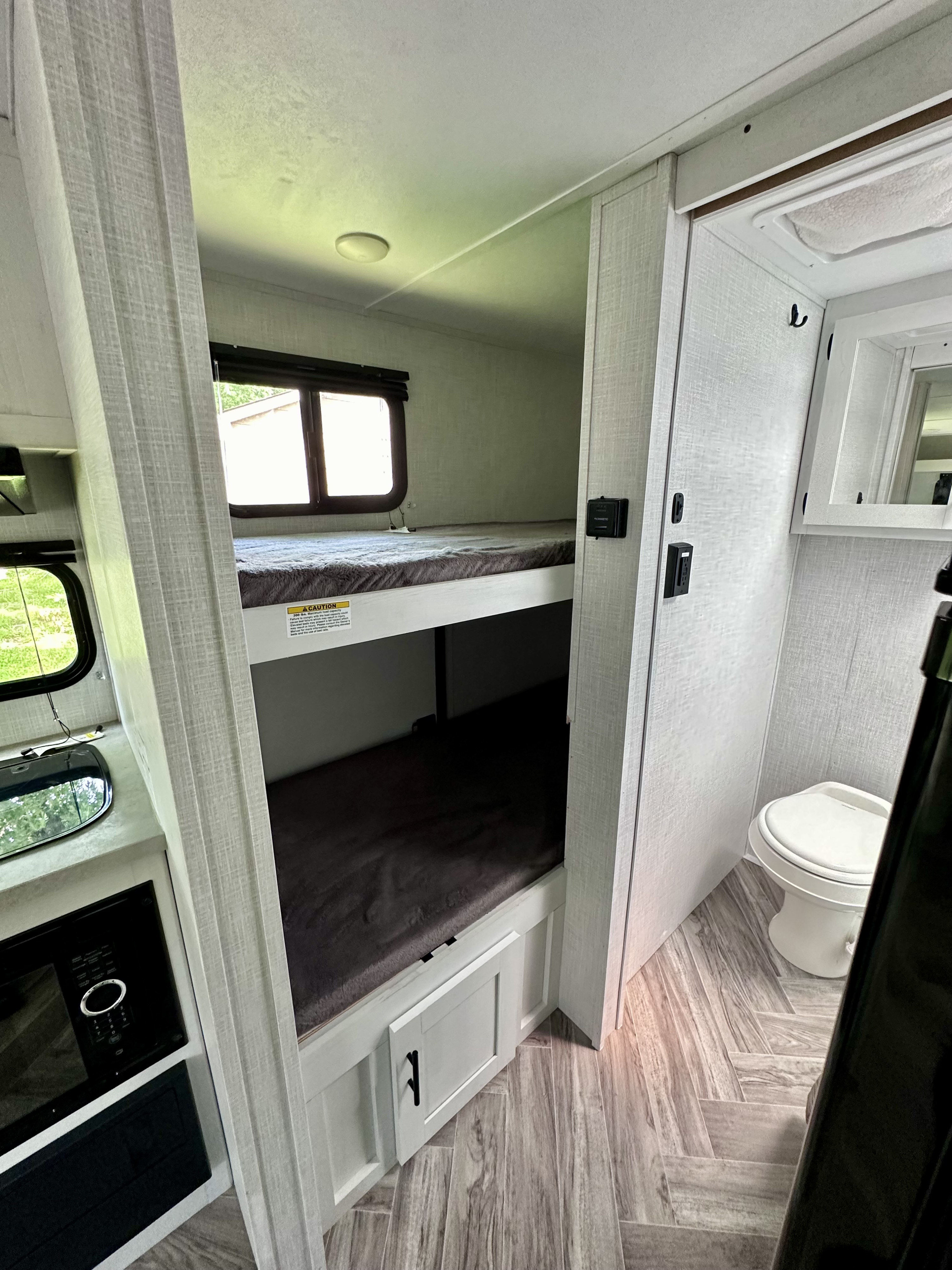 Inside an RV rental: cozy bunk beds, a compact kitchen counter with a microwave, and a toilet.. Dutchmen Coleman Rubicon 2023