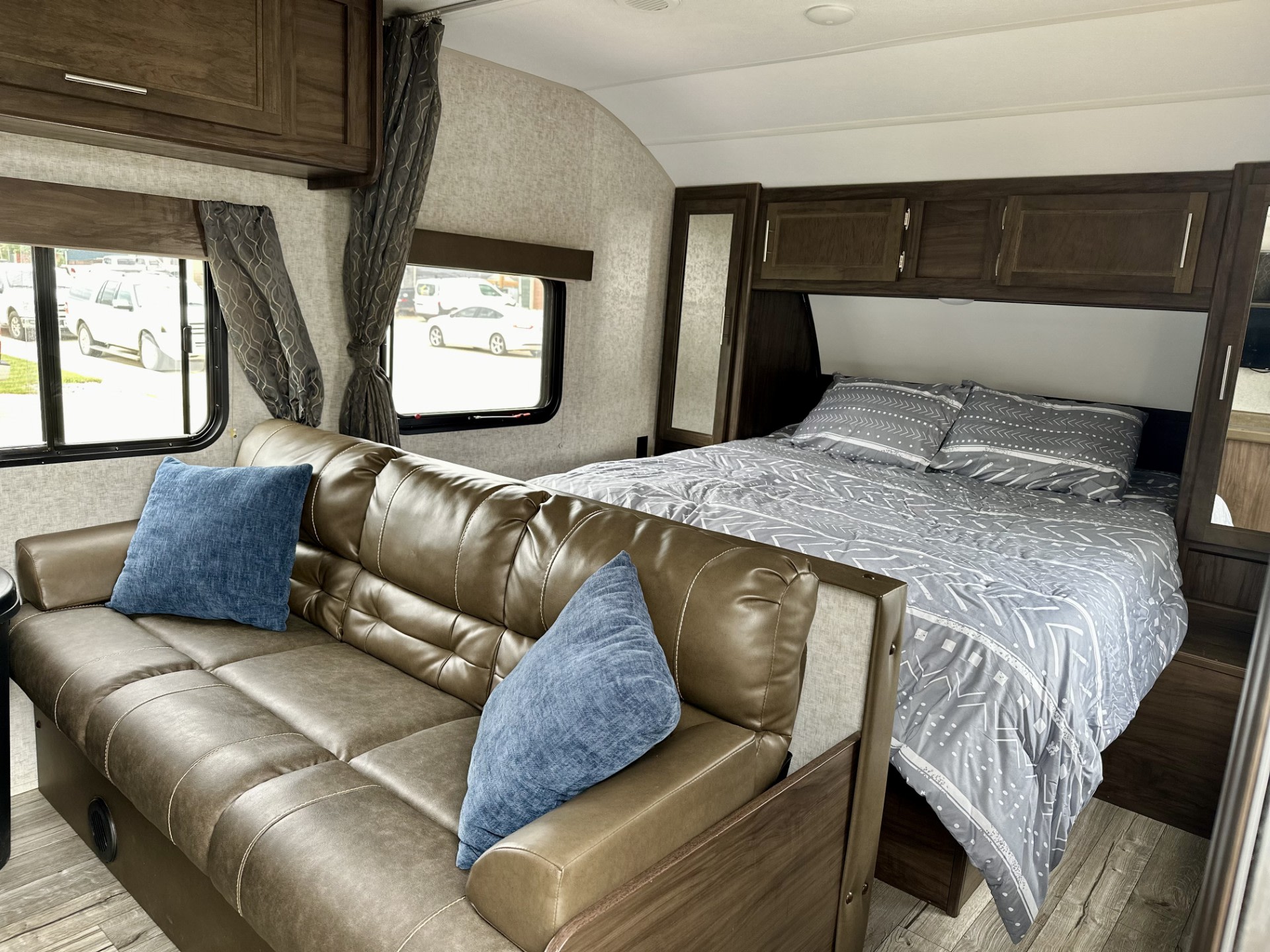 RV rental interior features a comfy brown couch with blue pillows and a bed with modern grey bedding. Ideal for travel.. Forest River Cherokee Grey Wolf Special Edition 2018