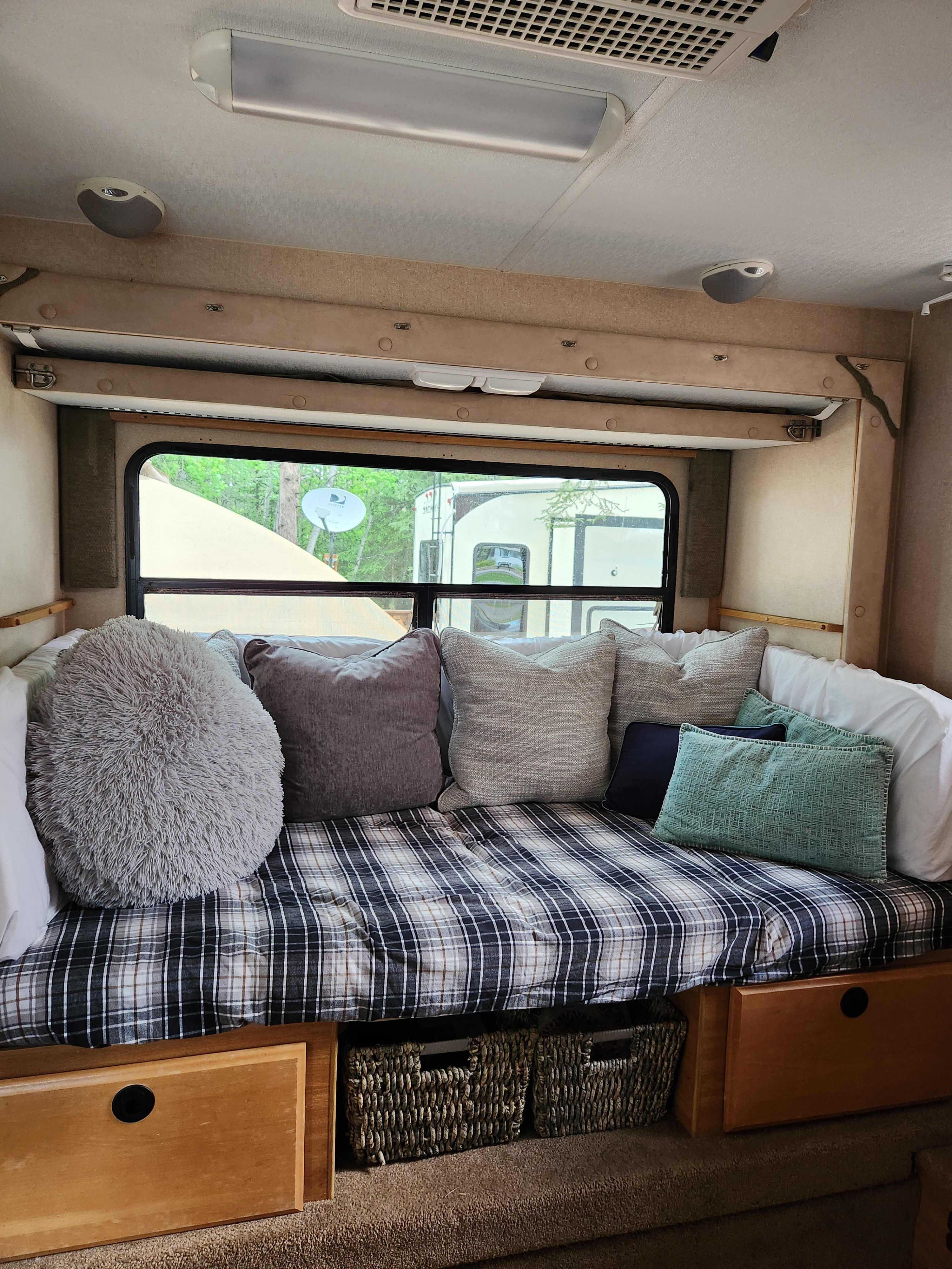 Cozy RV rental lounge area with plaid bedding, comfy pillows, and under-bed storage. Window view of nature & another RV.. Lance 1131 2007