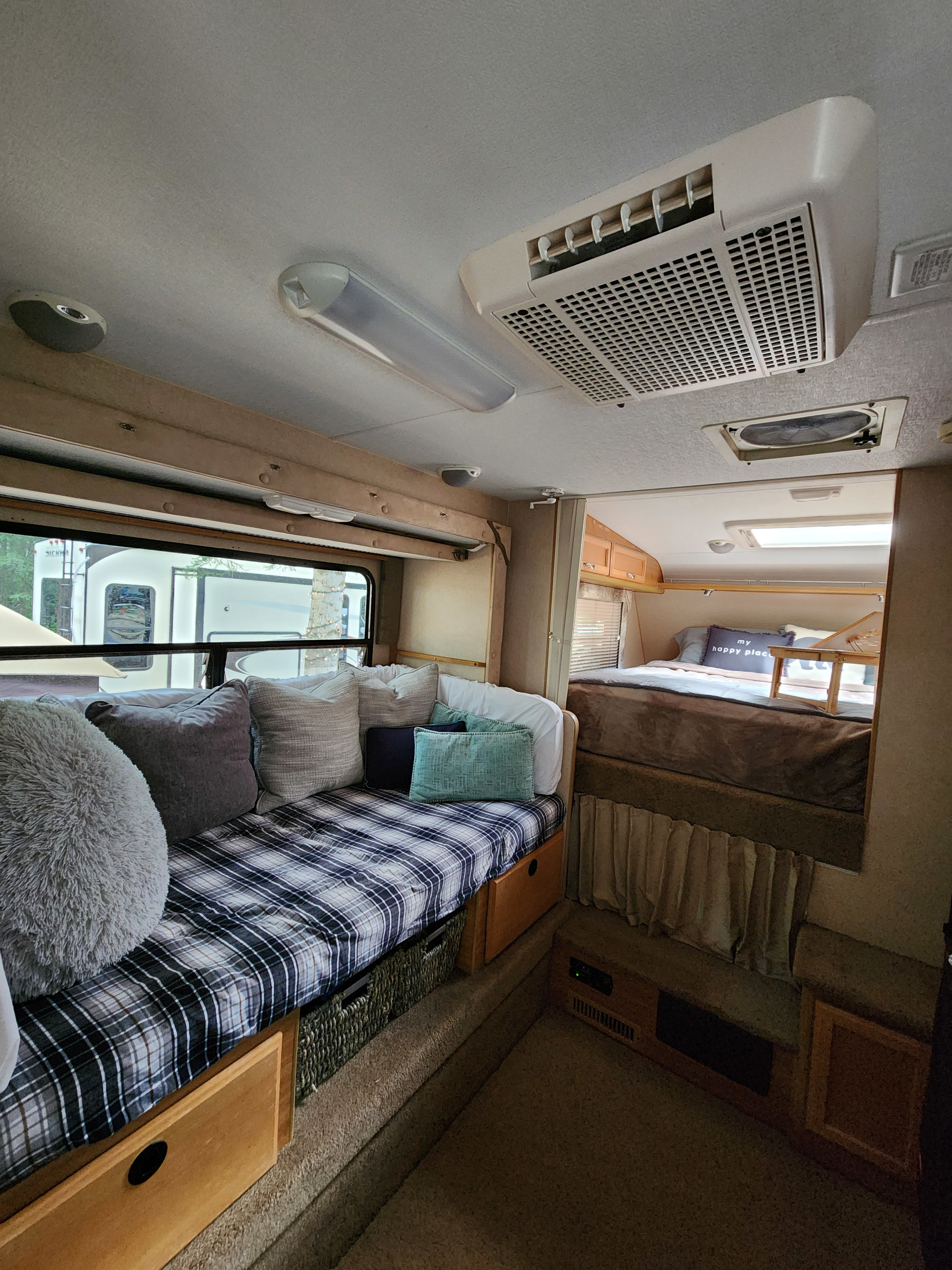 Step inside this cozy RV rental! Features plaid seating, a comfy raised bed, AC, and window views.. Lance 1131 2007