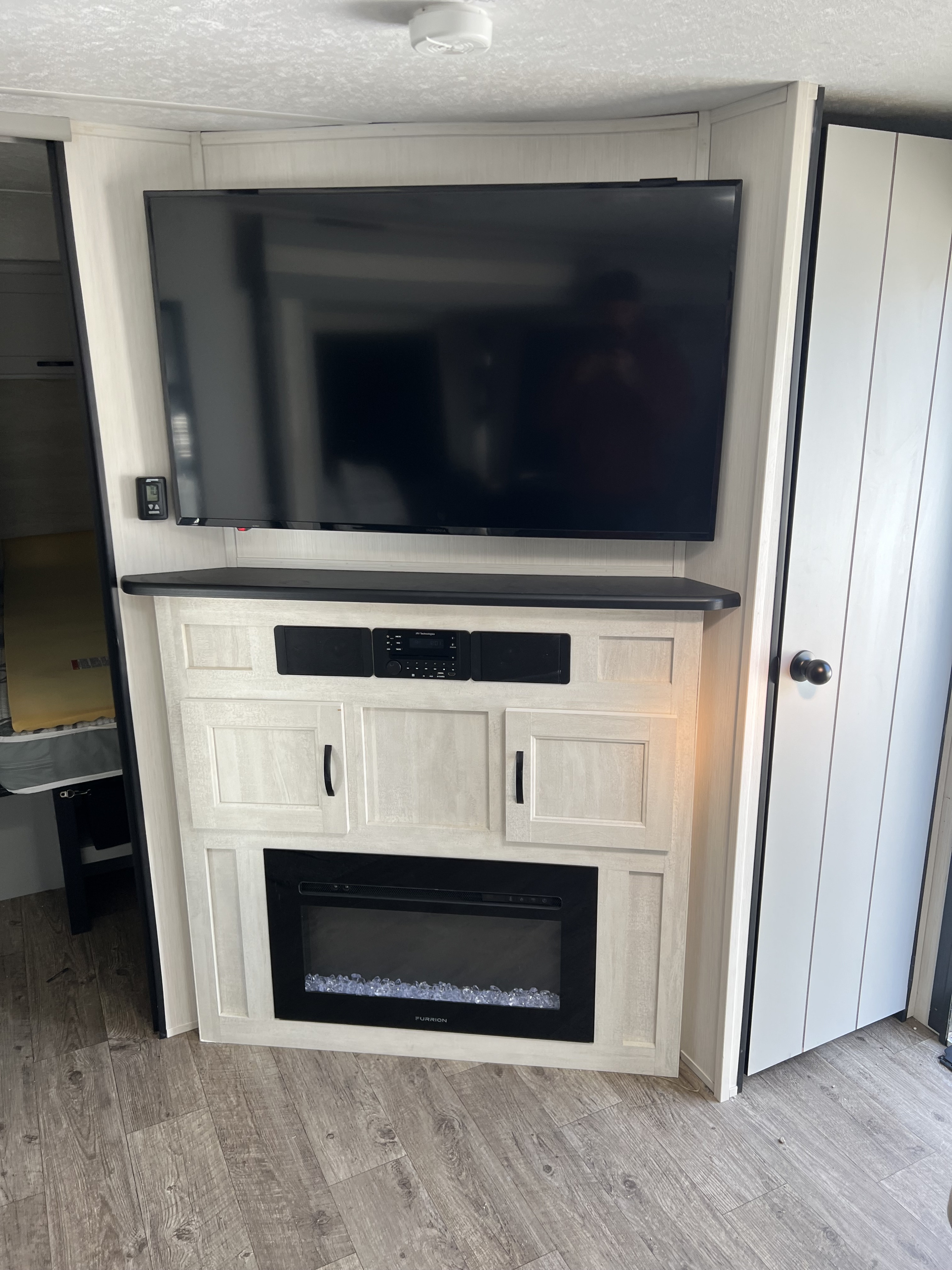 Modern RV rental features a built-in entertainment center with TV, stereo, and cozy electric fireplace in light wood cabinetry.. Forest River Vibe 2021