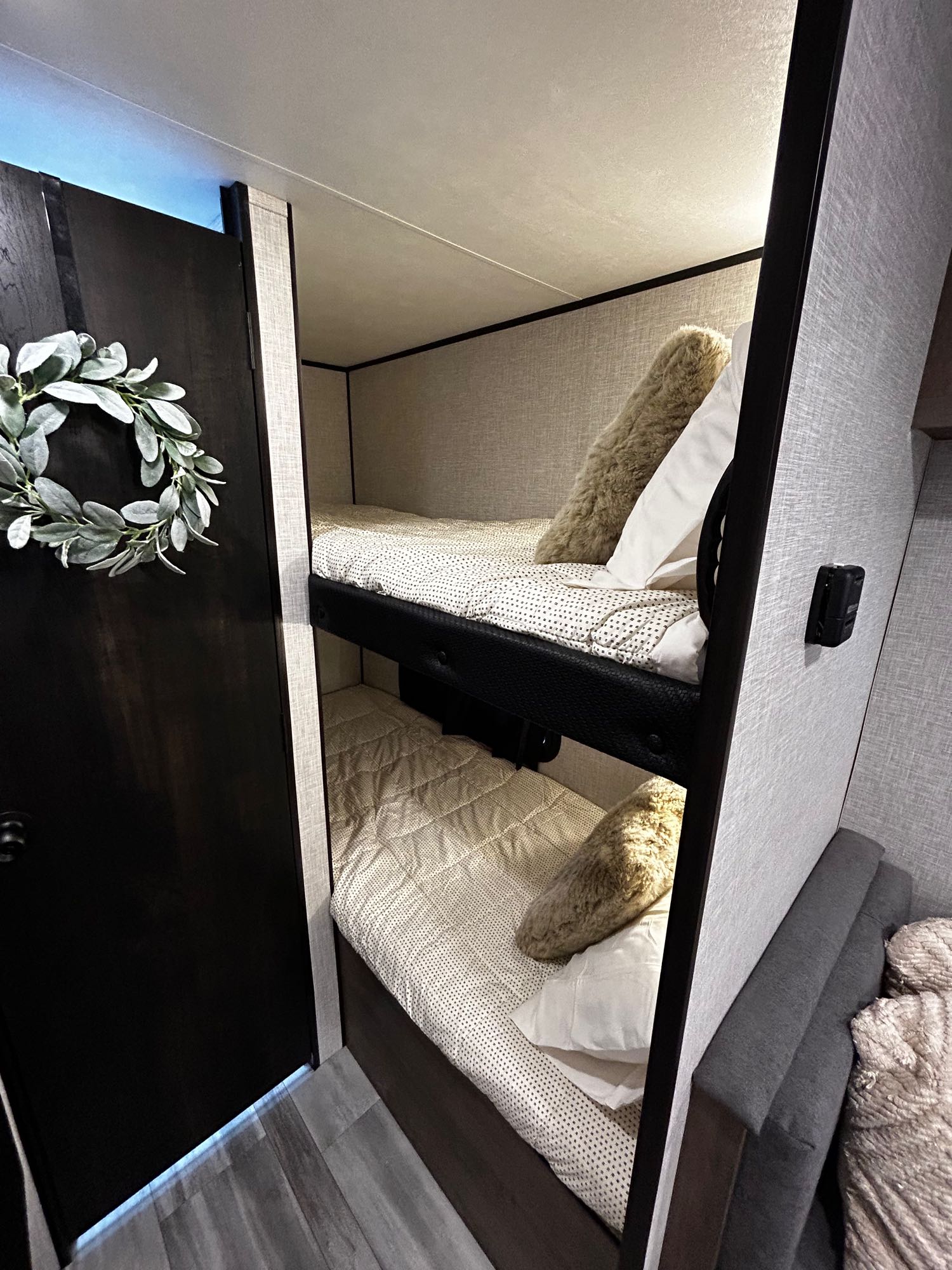 Cozy RV rental interior featuring two bunk beds with patterned bedding, a dark door with a wreath, and a sofa.. Jayco Jay Flight SLX Baja Edition 2024