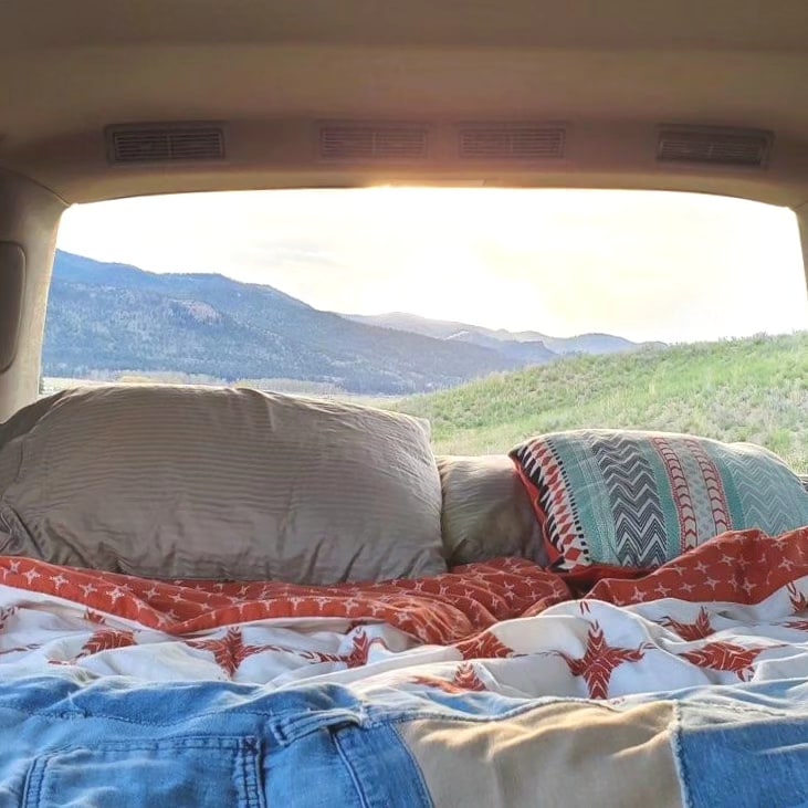 Cozy bed inside an RV rental, with pillows & blankets, looking out at a stunning mountain view through the rear window.. Chevrolet Astro 1999