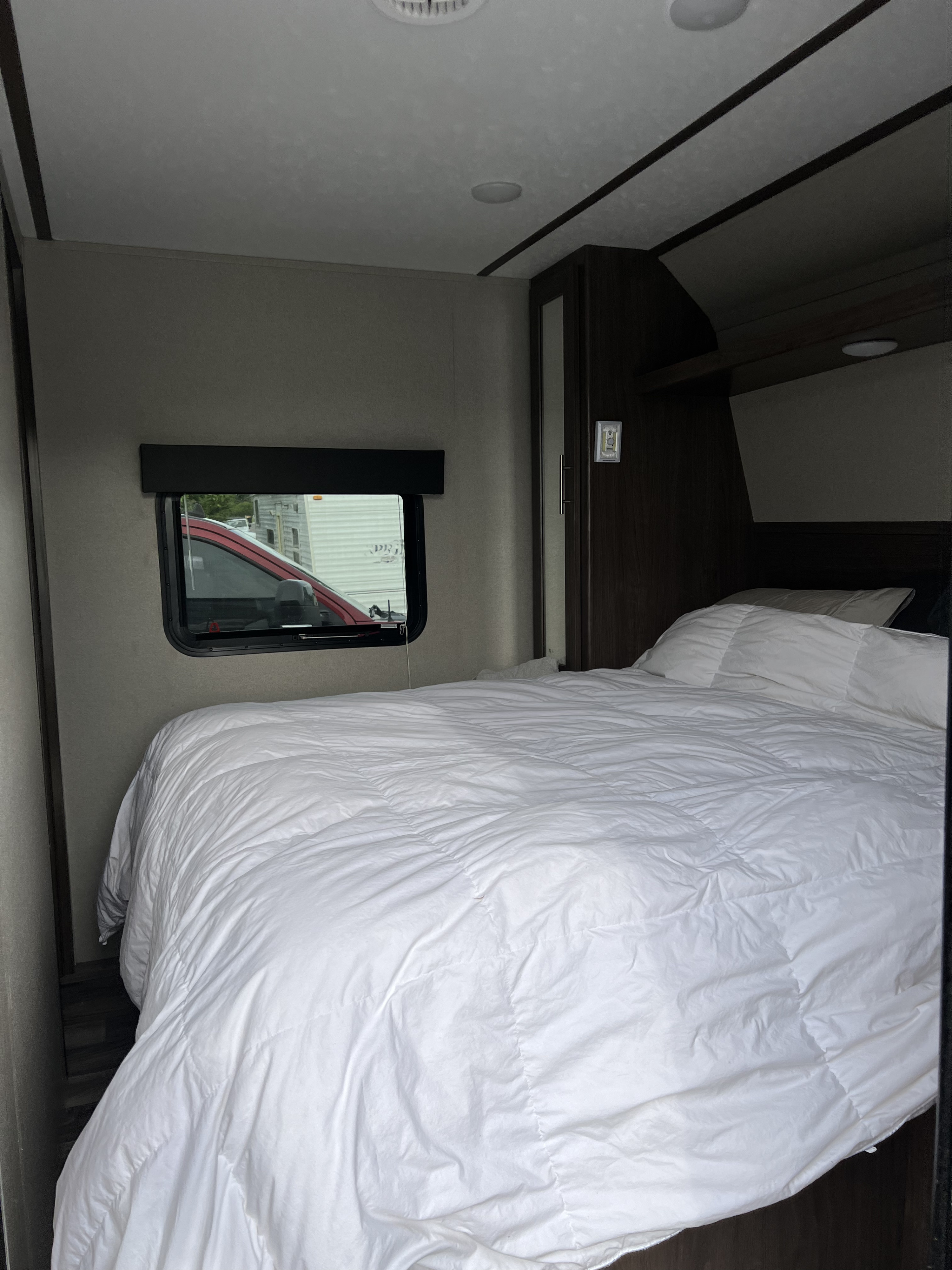 Inside an RV rental: a neat bedroom with a large white bed, window view, and built-in storage.. Keystone RV Hideout Luxury 2020