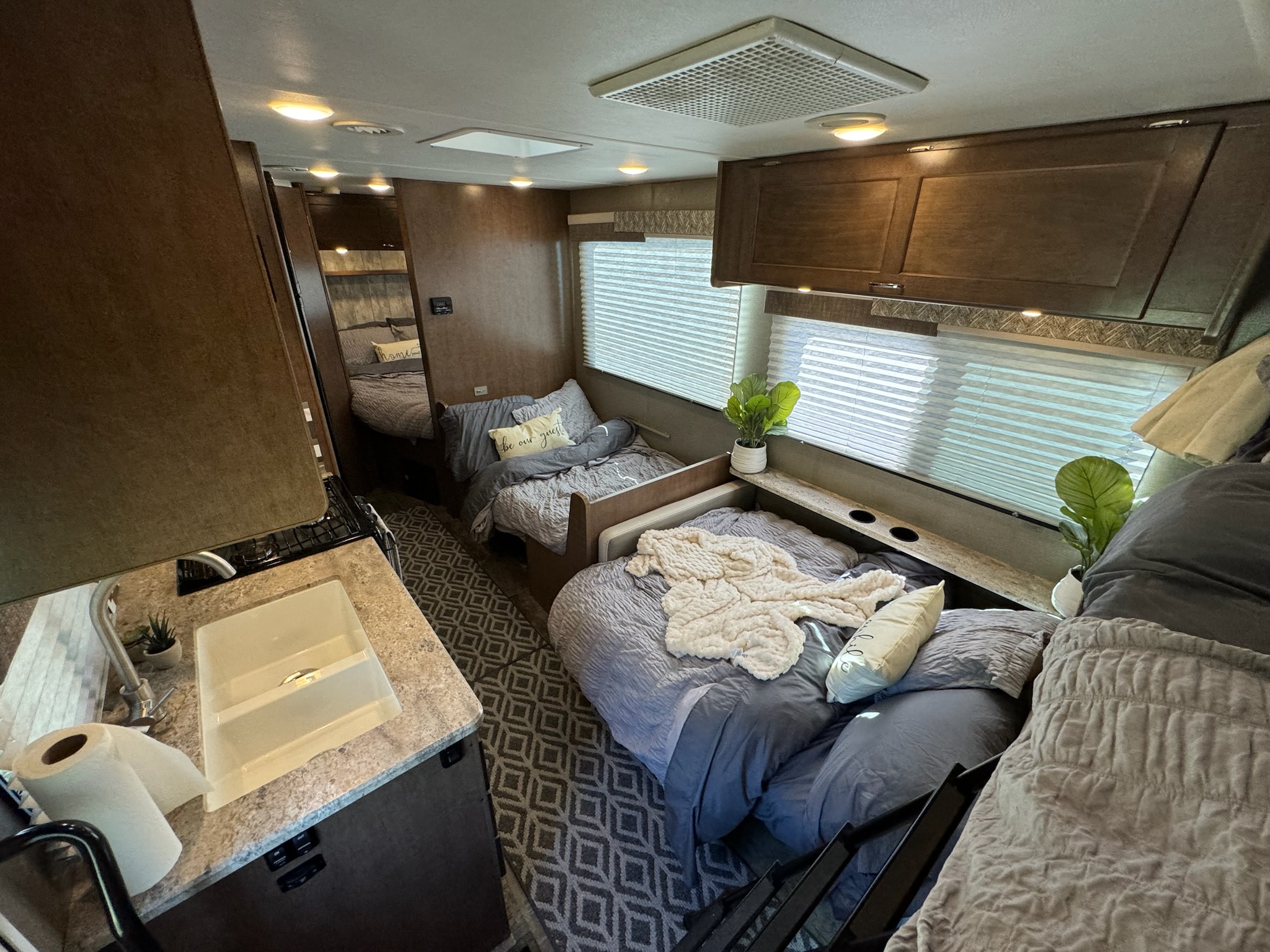 Inside an RV rental: multiple bunk beds, a small kitchen counter with sink, and overhead cabinets offer a cozy setup.. Winnebago Outlook 2019