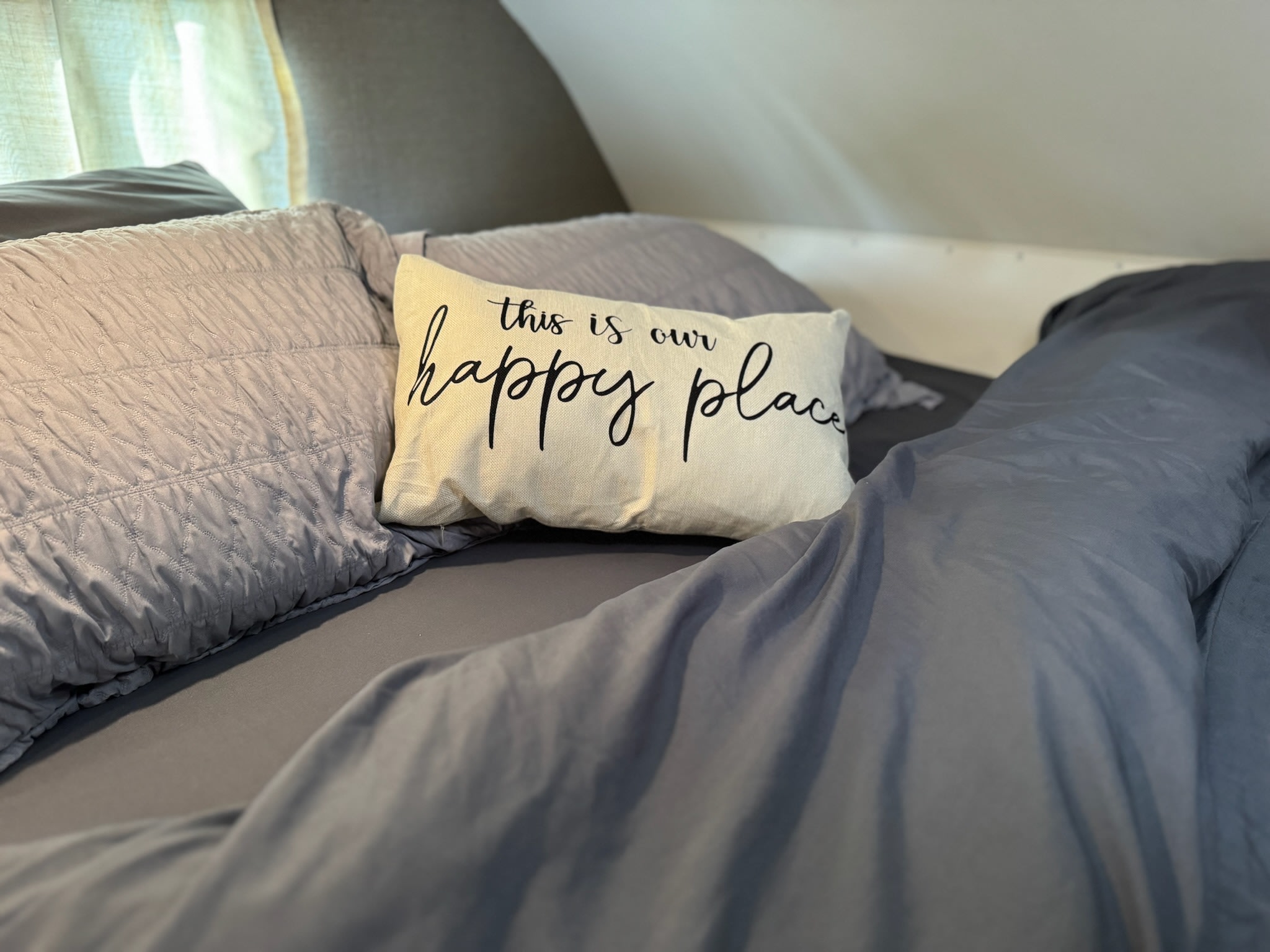 Cozy grey bed in an RV rental, with a cream "happy place" pillow. Perfect for road trip comfort.. Winnebago Outlook 2019