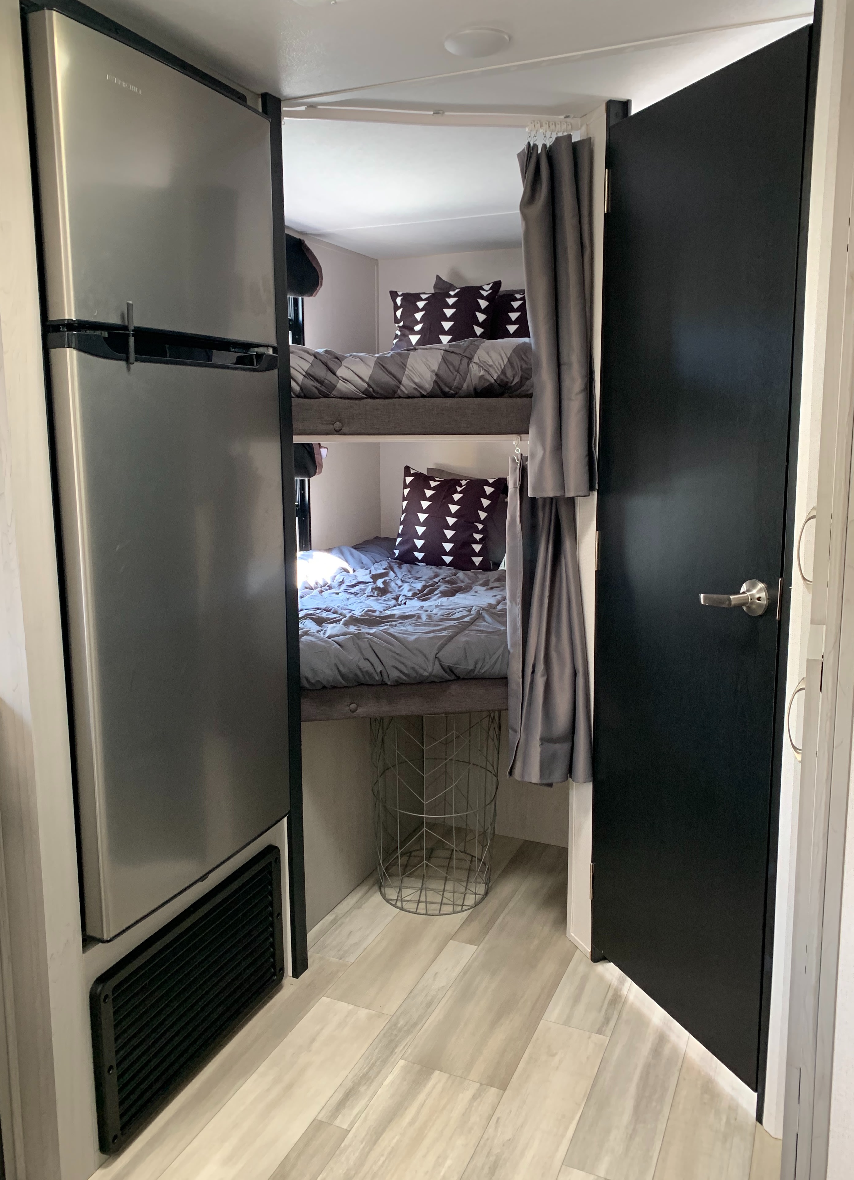 Inside a modern RV rental: gray bunk beds with patterned pillows, a sleek fridge, and a dark door.. Tracer 24 DBS 2022
