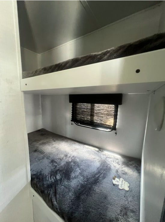 RV rental bunk beds with soft grey bedding, ideal for travel. Lower bunk has a window with blinds.. Keystone RV Hideout 2023