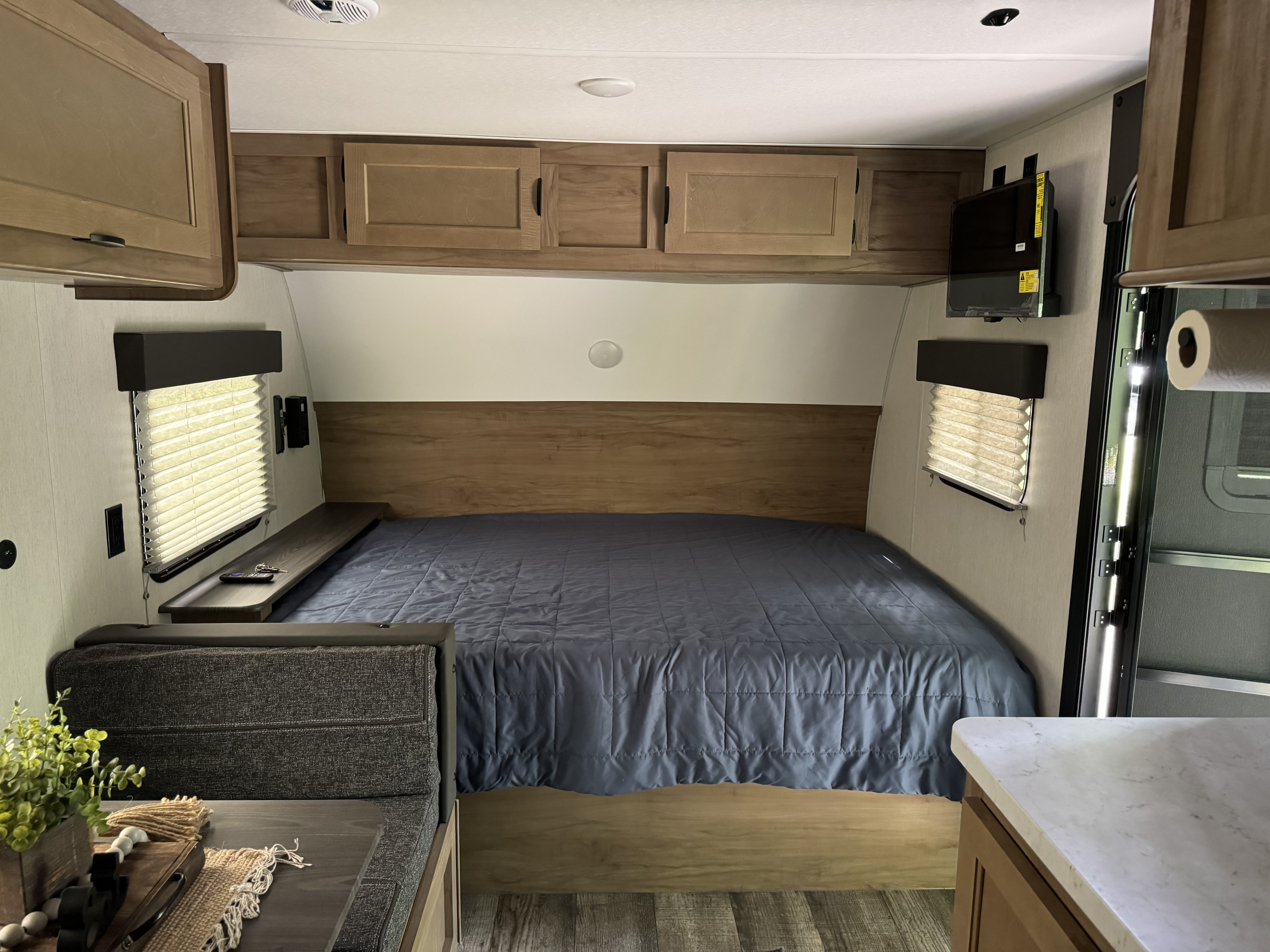 Inside an RV rental: a compact bedroom with a cozy bed, overhead cabinets, window, and TV.. Forest River Cherokee Wolf Pup 2023