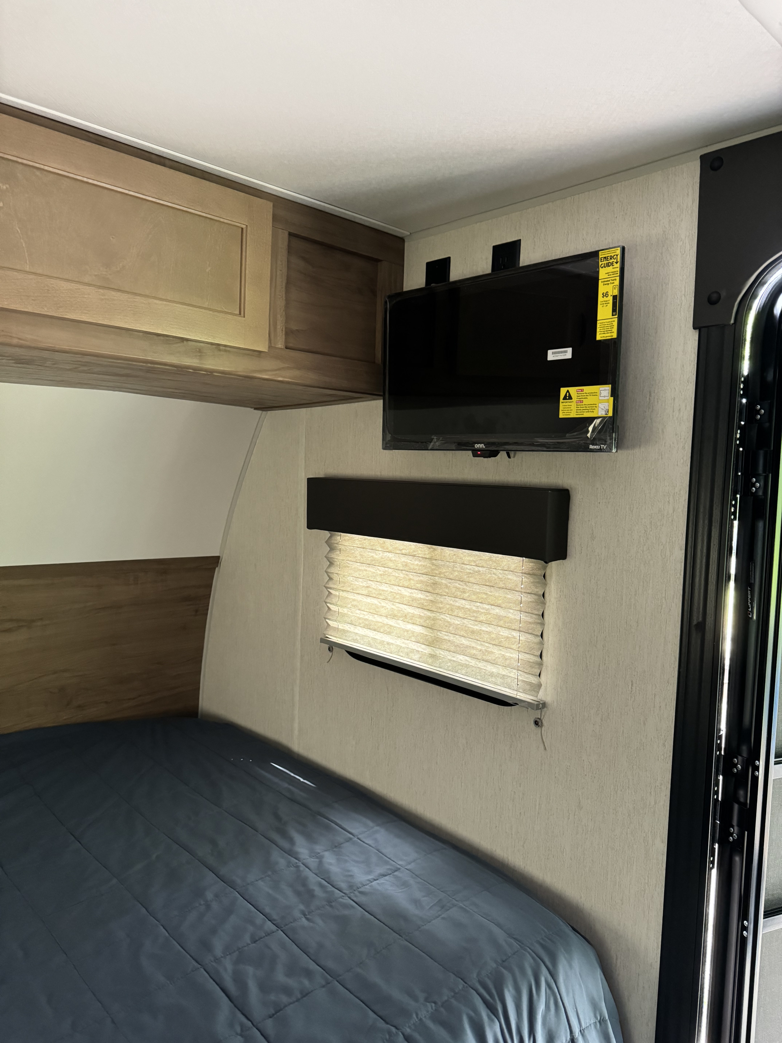 Cozy RV rental bedroom view: includes a dark bed, wooden cabinets, and a wall-mounted Onn. Roku TV with energy label.. Forest River Cherokee Wolf Pup 2023