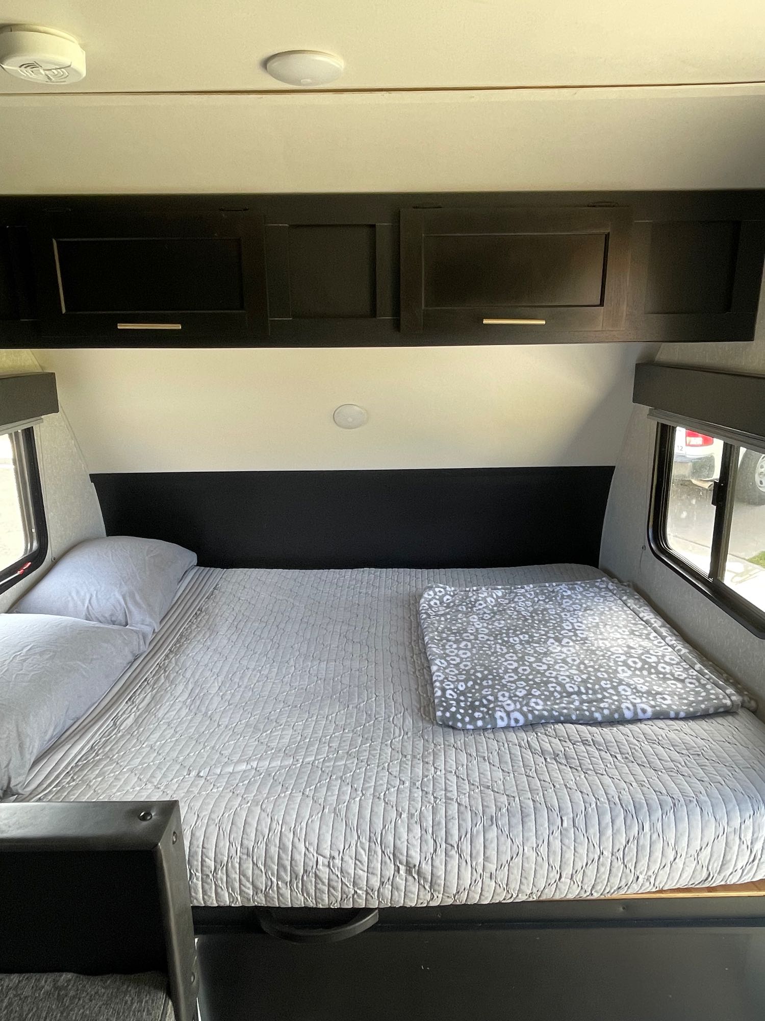 This RV rental bedroom features a comfortable bed with quilted covers, dark overhead cabinets, and side windows.. Forest River Cherokee Wolf Pup 2022