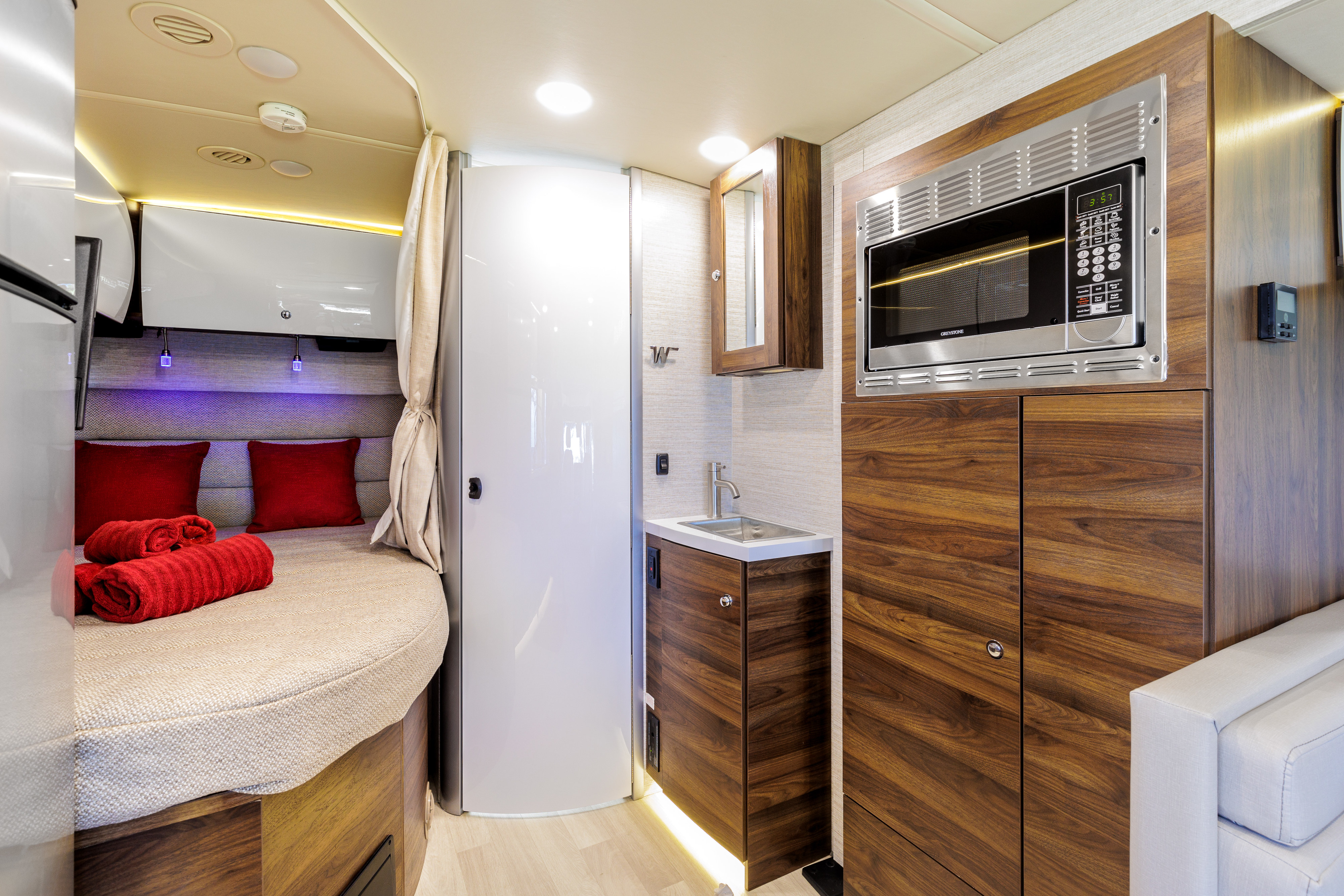 Modern RV rental interior with a cozy bedroom, microwave, sink, and stylish wooden cabinetry, offering comfortable travel.. Winnebago View 2023