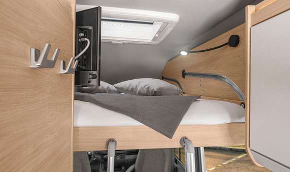 Explore your RV rental! This image features a bright, compact camper bunk bed with a TV, cozy bedding, reading lamp, and coat hooks.. Knaus Boxdrive XL 2024