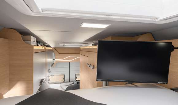 Explore this comfy RV rental bedroom featuring a flat-screen TV, modern wood cabinetry, and ample lighting.. Knaus Boxdrive XL 2024