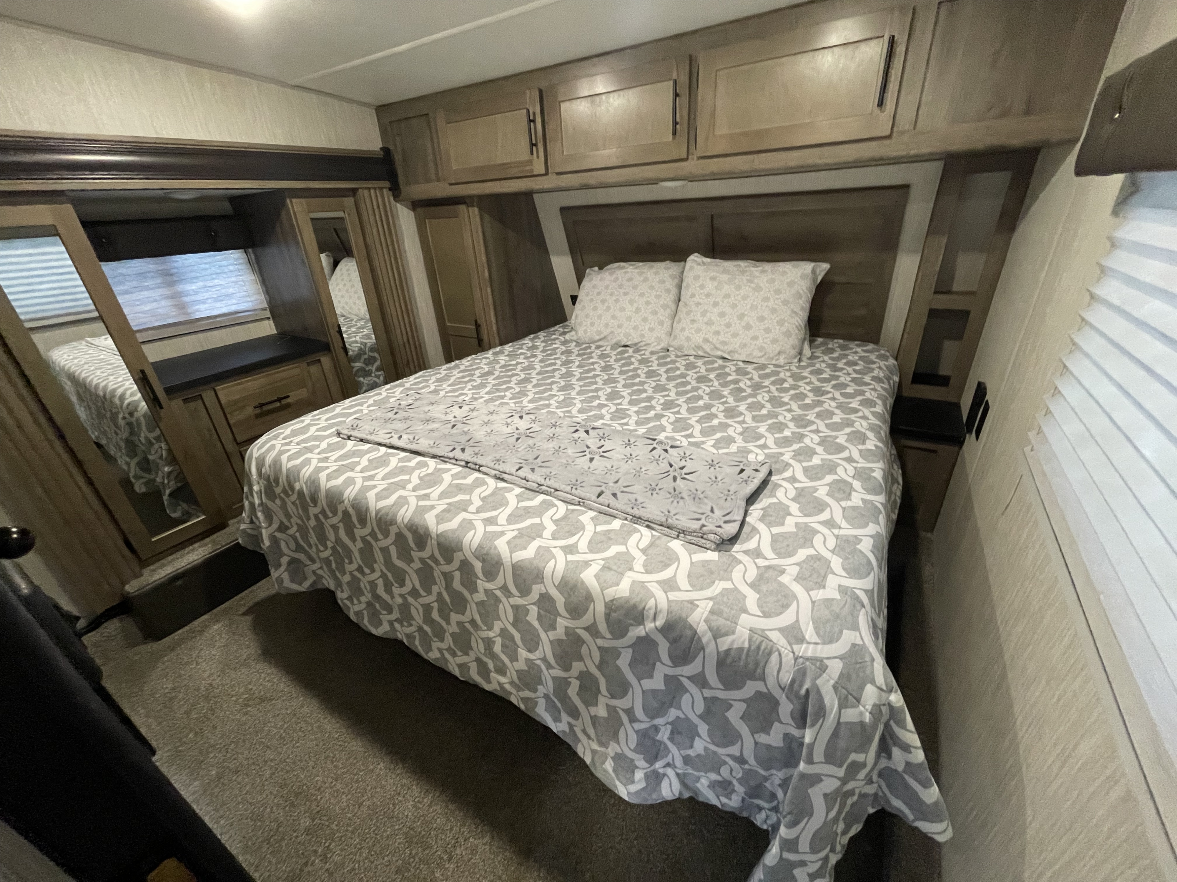 Cozy RV rental bedroom with patterned bedding, overhead cabinets, and a mirrored wardrobe.. Forest River Vengeance 2020