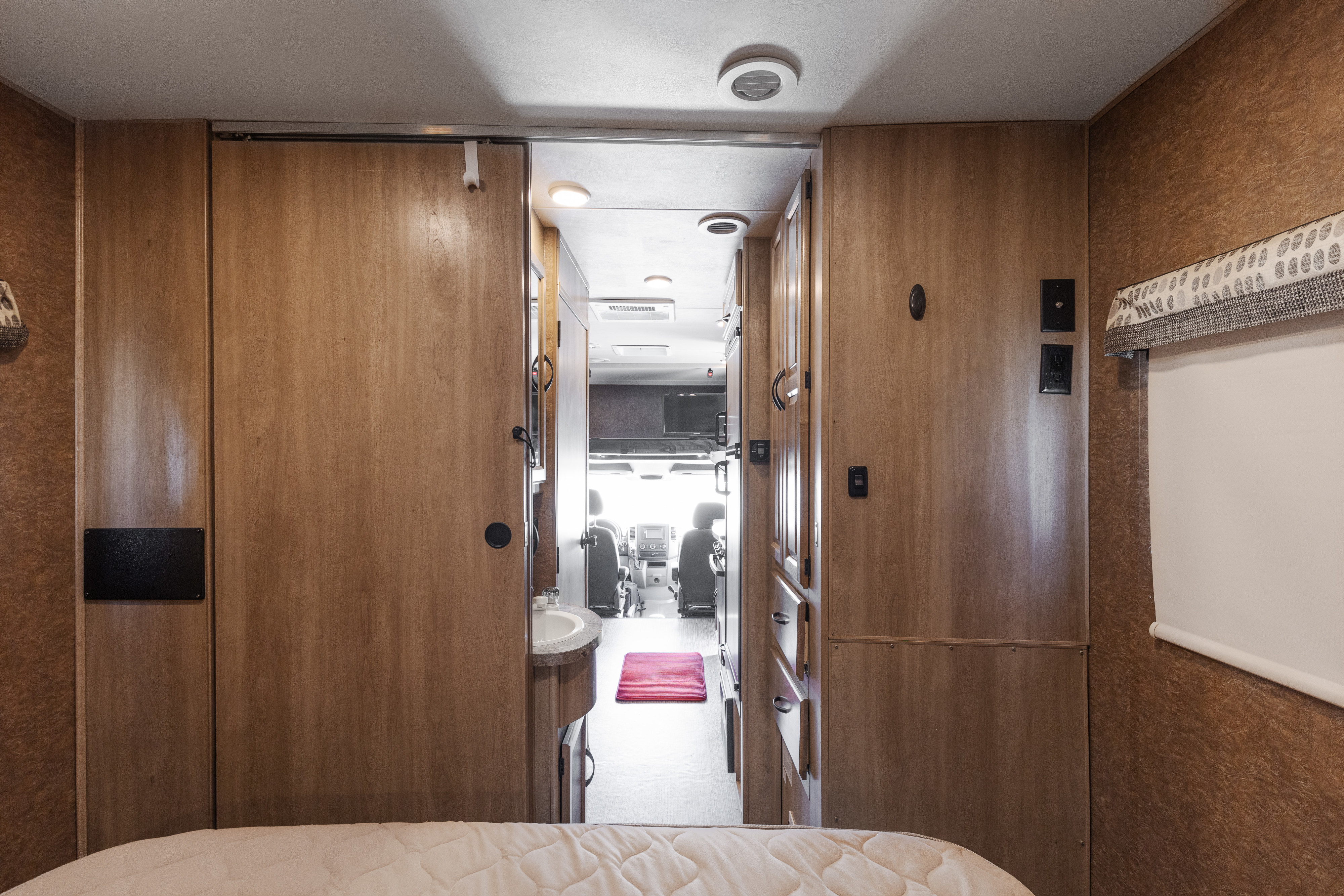 View from the bedroom of this rv rental, revealing the bathroom vanity and the cockpit area for comfortable travel.. Coachmen Prism Select 2018