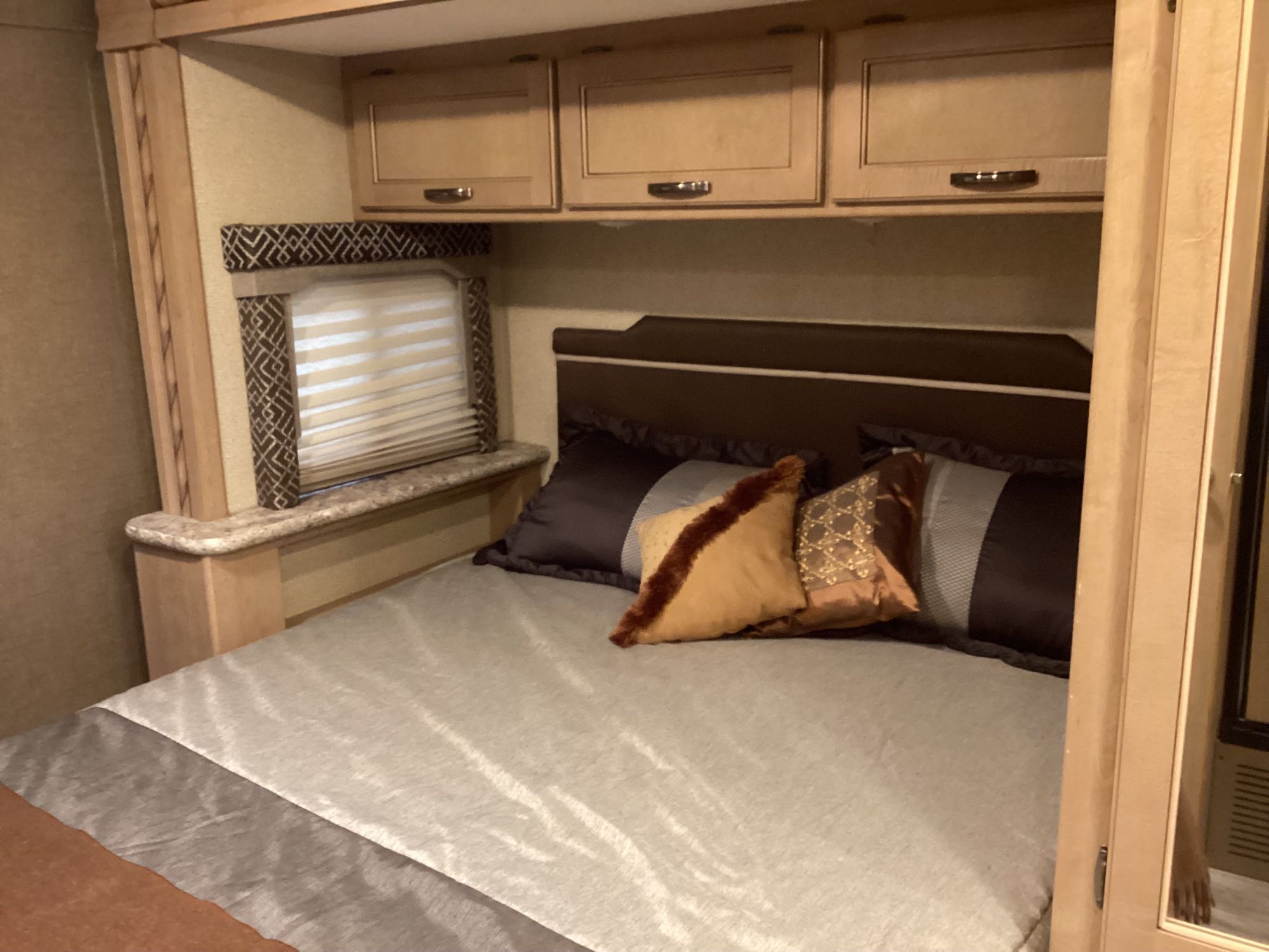 Cozy RV rental bedroom with a comfortable bed, overhead cabinets, and window blinds for your next adventure.. Thor Freedom Elite 2018