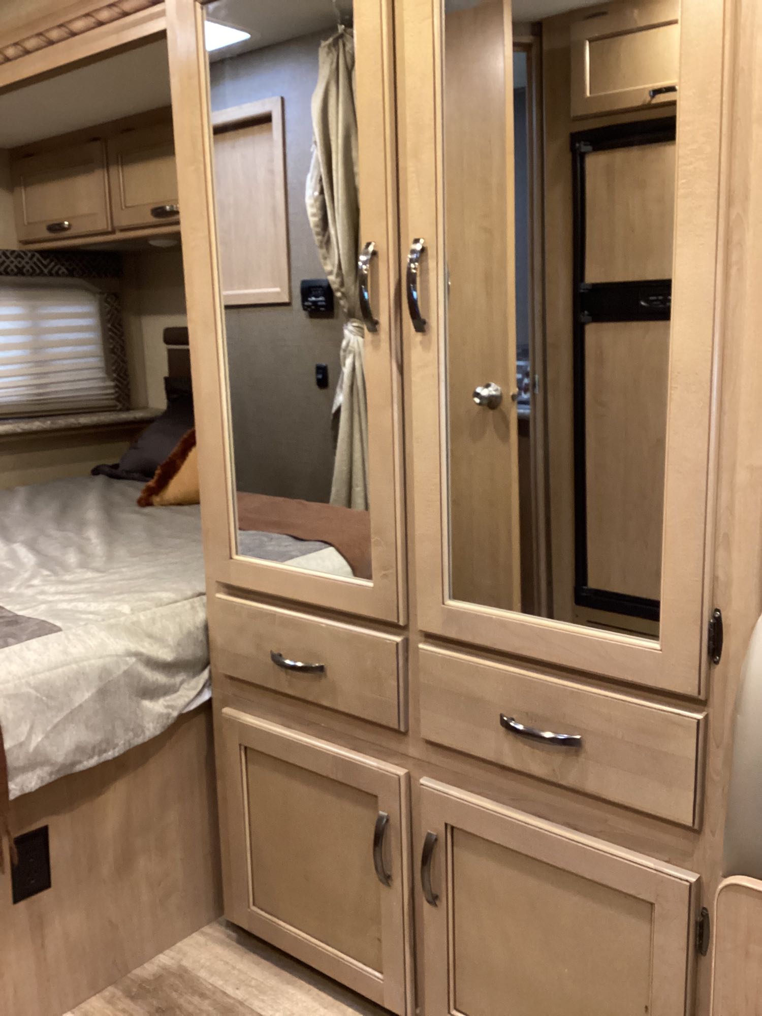 Inside an RV rental: a compact bedroom with a bed, light wood cabinets, mirrored doors, and drawers for storage.. Thor Freedom Elite 2018