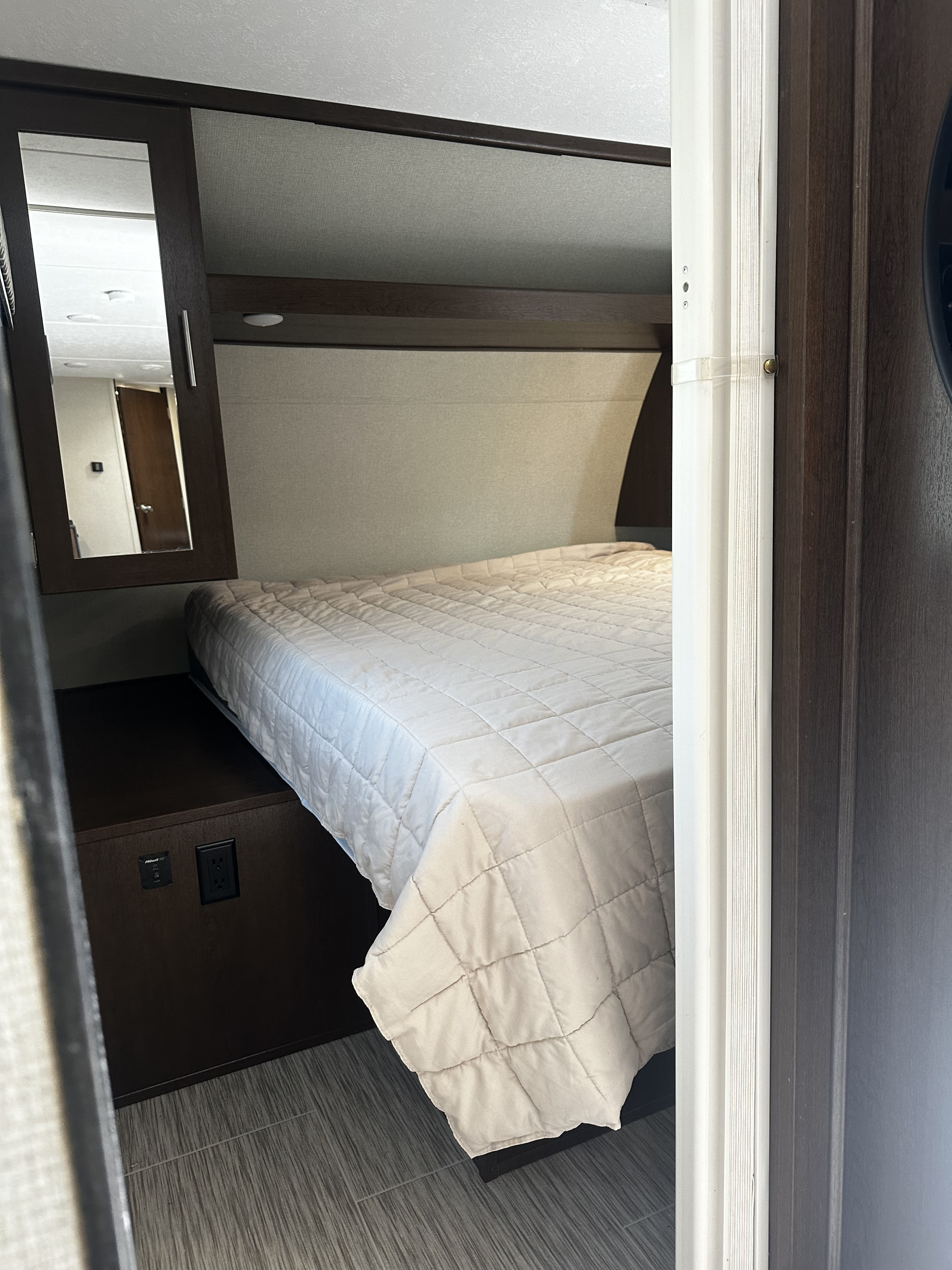 Inside an RV rental: a compact bedroom with a cozy bed, mirrored storage, power outlets, and modern finishes.. Forest River Tracer Breeze 2018