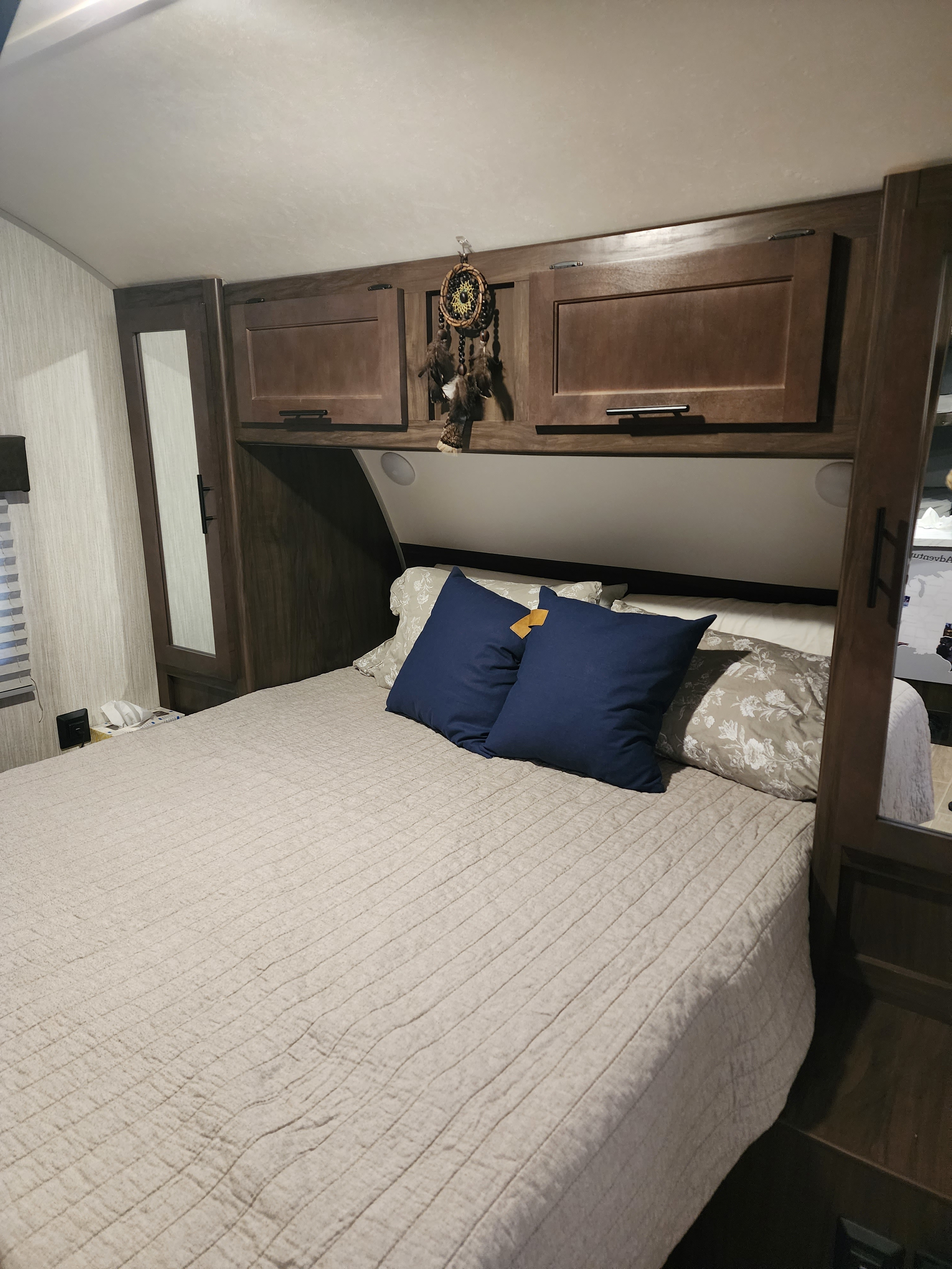 Cozy RV rental bedroom with a quilted bed, blue pillows, and wooden overhead cabinets, offering a comfortable space.. Forest River Cherokee Grey Wolf Special Edition 2021