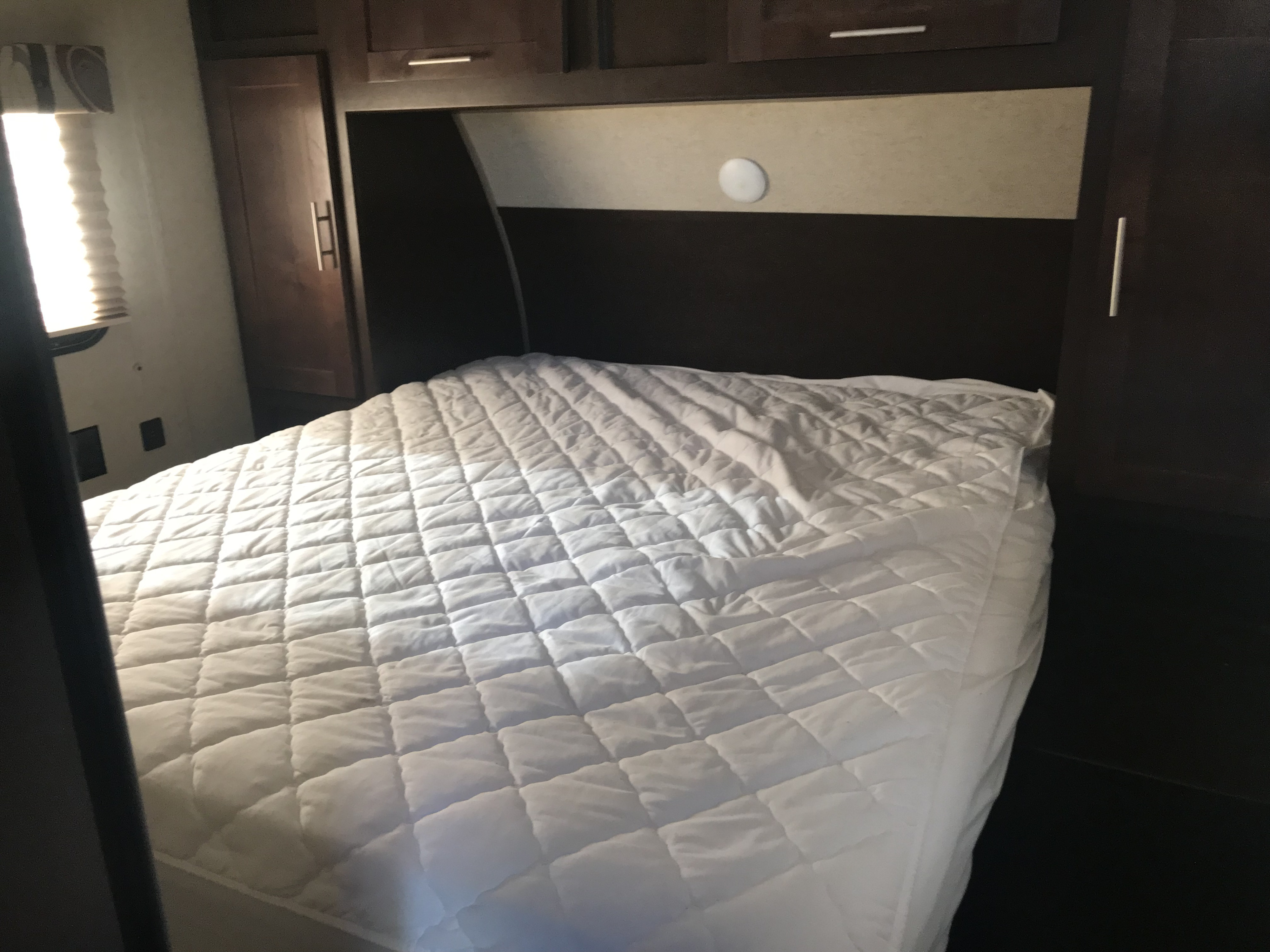 Inside an RV rental bedroom: a neatly made bed with a white quilted mattress pad, flanked by dark wood cabinets.. Forest River Cherokee Grey Wolf Toy Hauler 2016