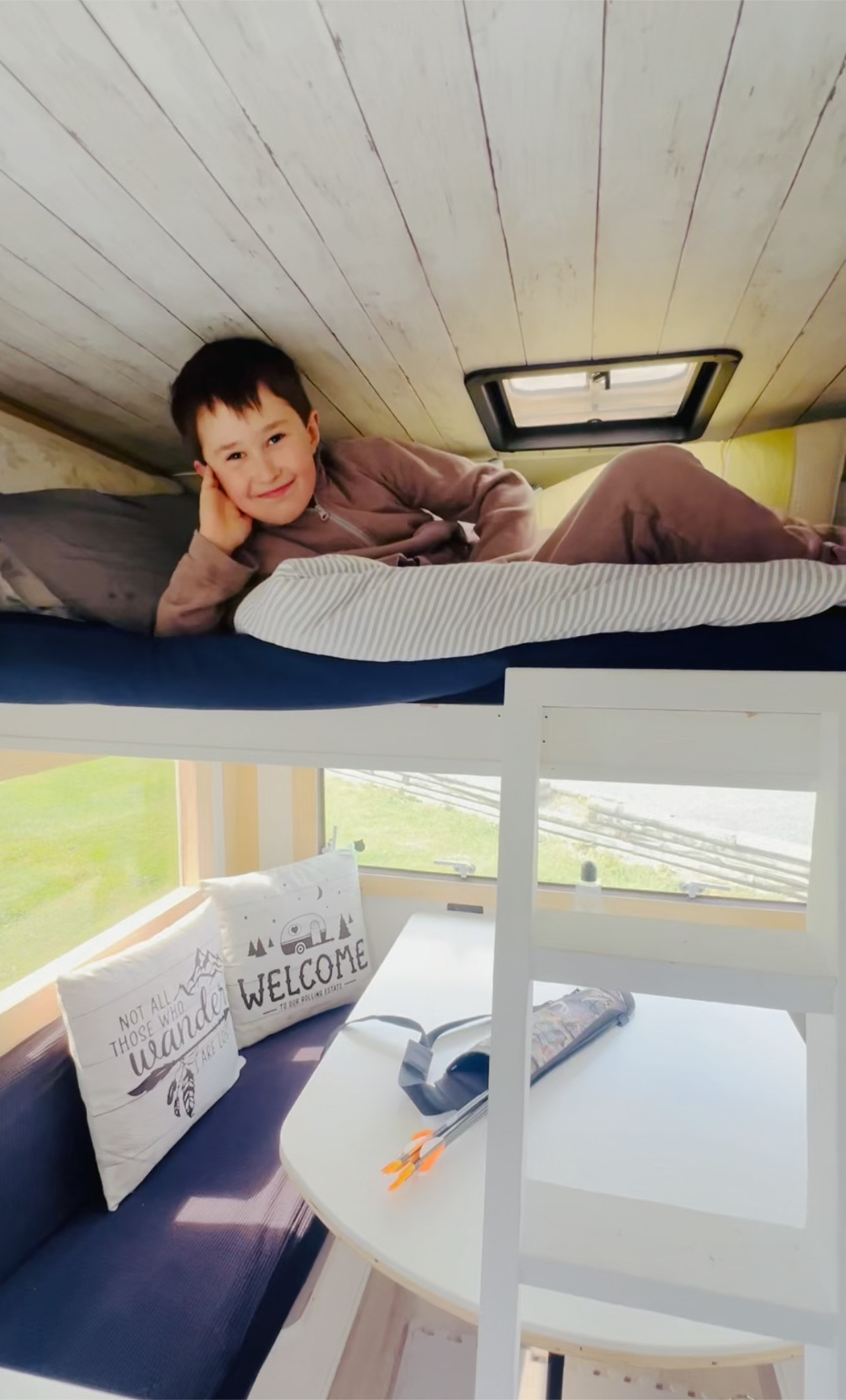 An RV rental's cozy bunk bed, where a happy child smiles. Below, a dinette with themed pillows and outdoor views.. Other Other 1985