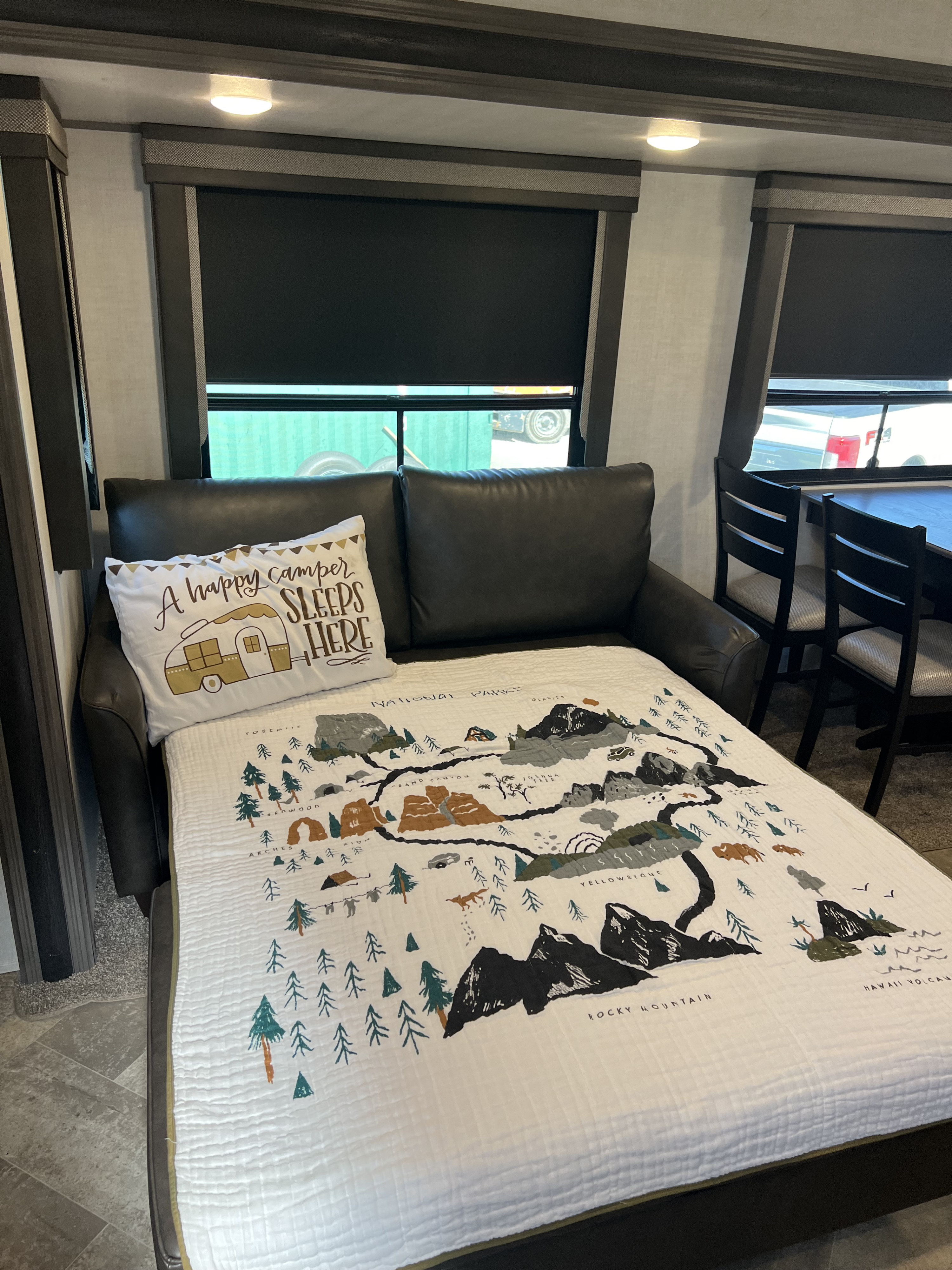 RV rental interior featuring a comfy pull-out bed with a "happy camper" pillow and National Parks map blanket. Perfect for travel!. Alta 2850KRL 2021
