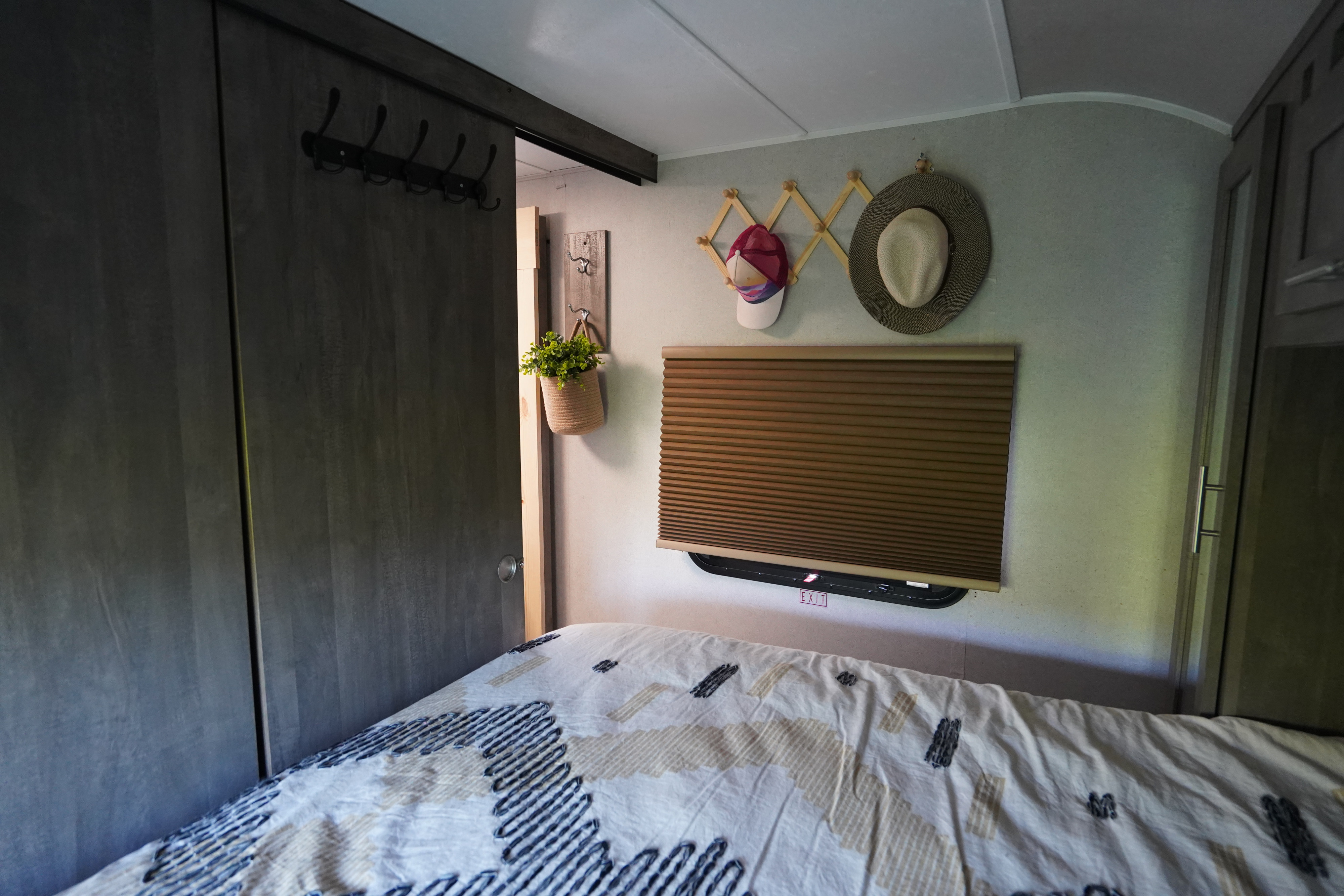 RV rental bedroom: patterned bed, window with blind & exit sign, and wall storage with hooks.. Forest River Vibe 2020