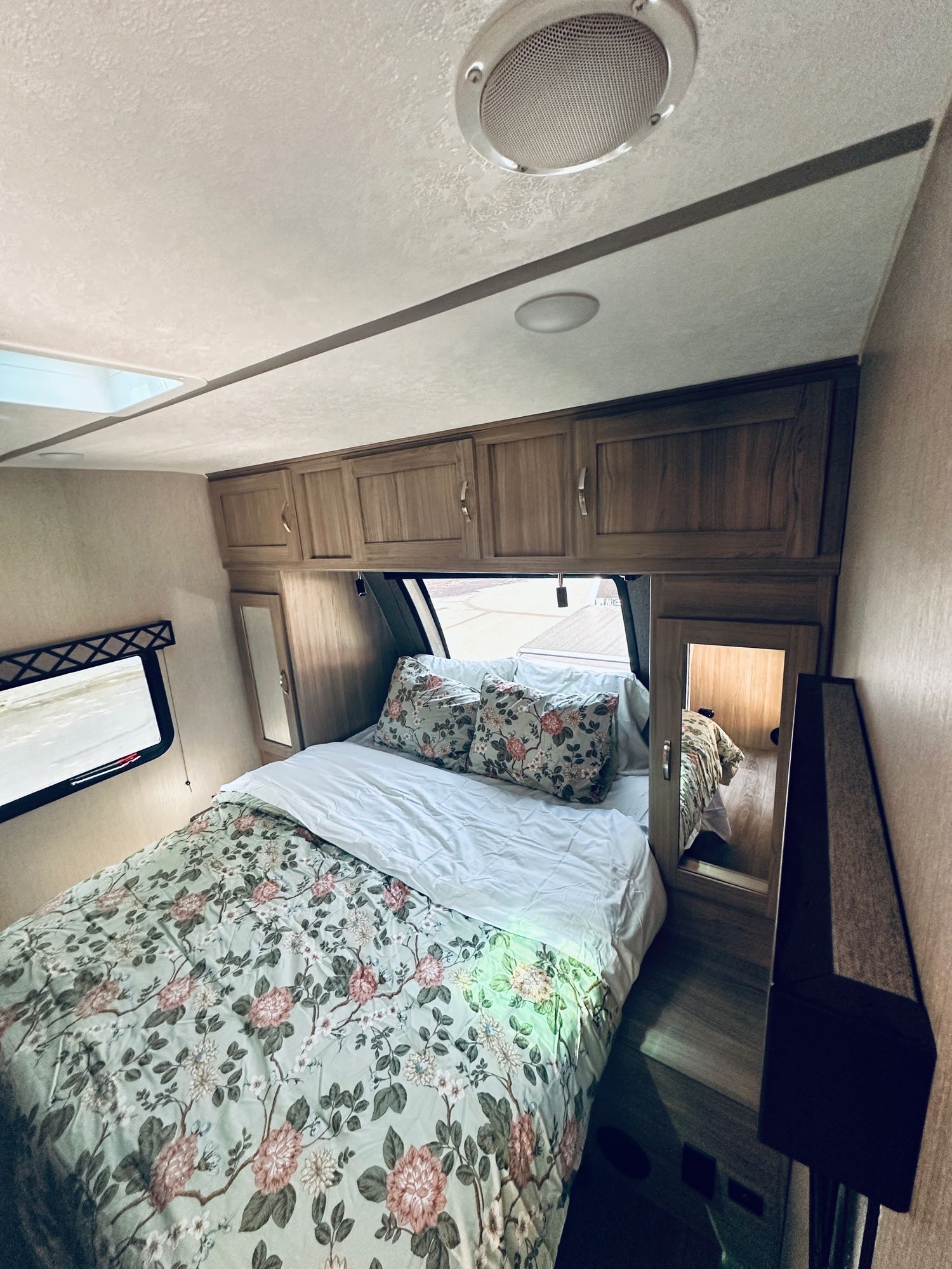 This RV rental bedroom features a comfy bed with floral bedding, overhead cabinets, and mirrored wardrobes. Relaxing sleeping space!. Coachmen Freedom Express Ultra Lite 2021