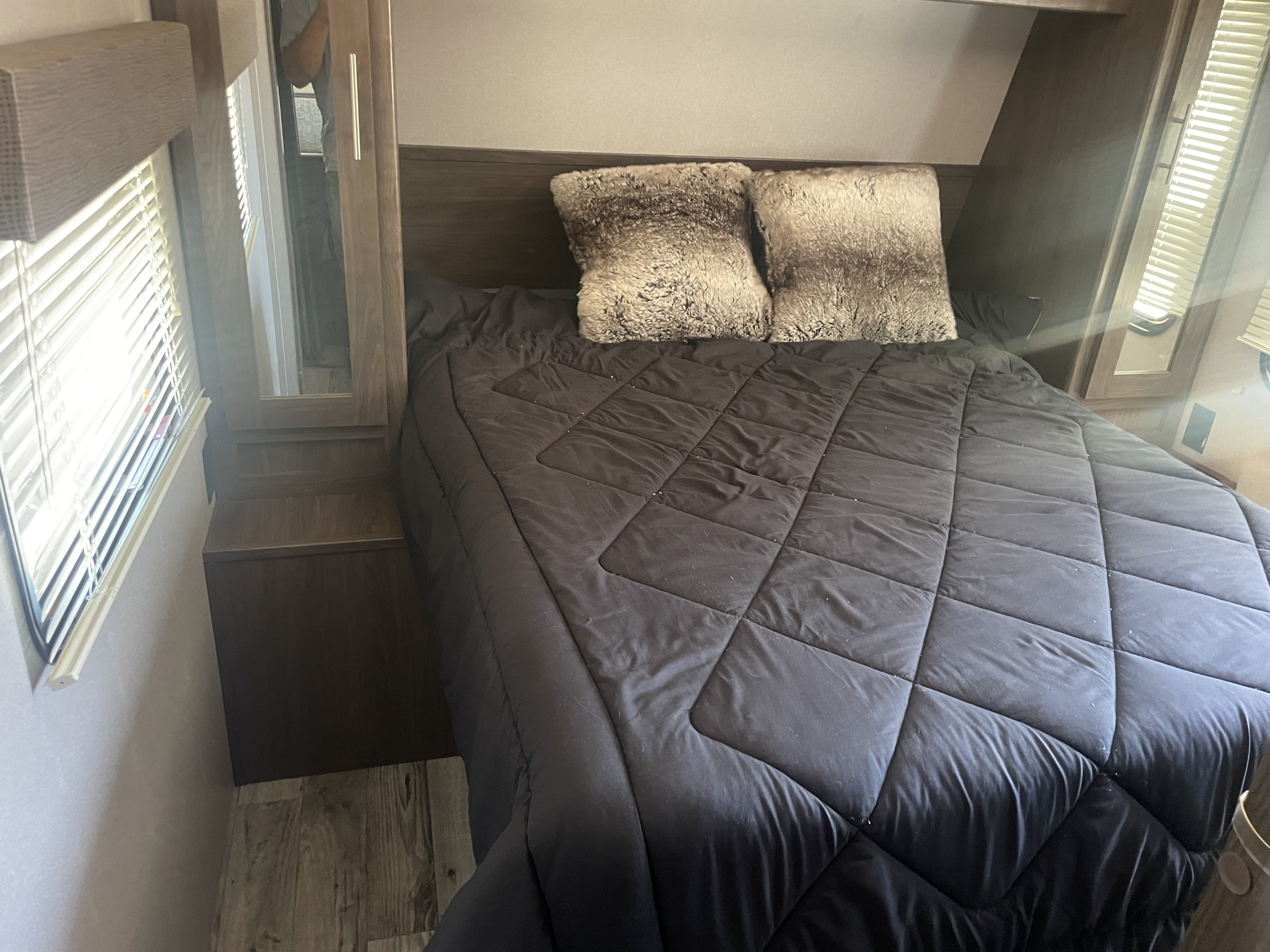 This RV rental shows a compact bedroom with a bed featuring dark bedding and two fluffy decorative pillows.. Keystone RV Hideout LHS 2019