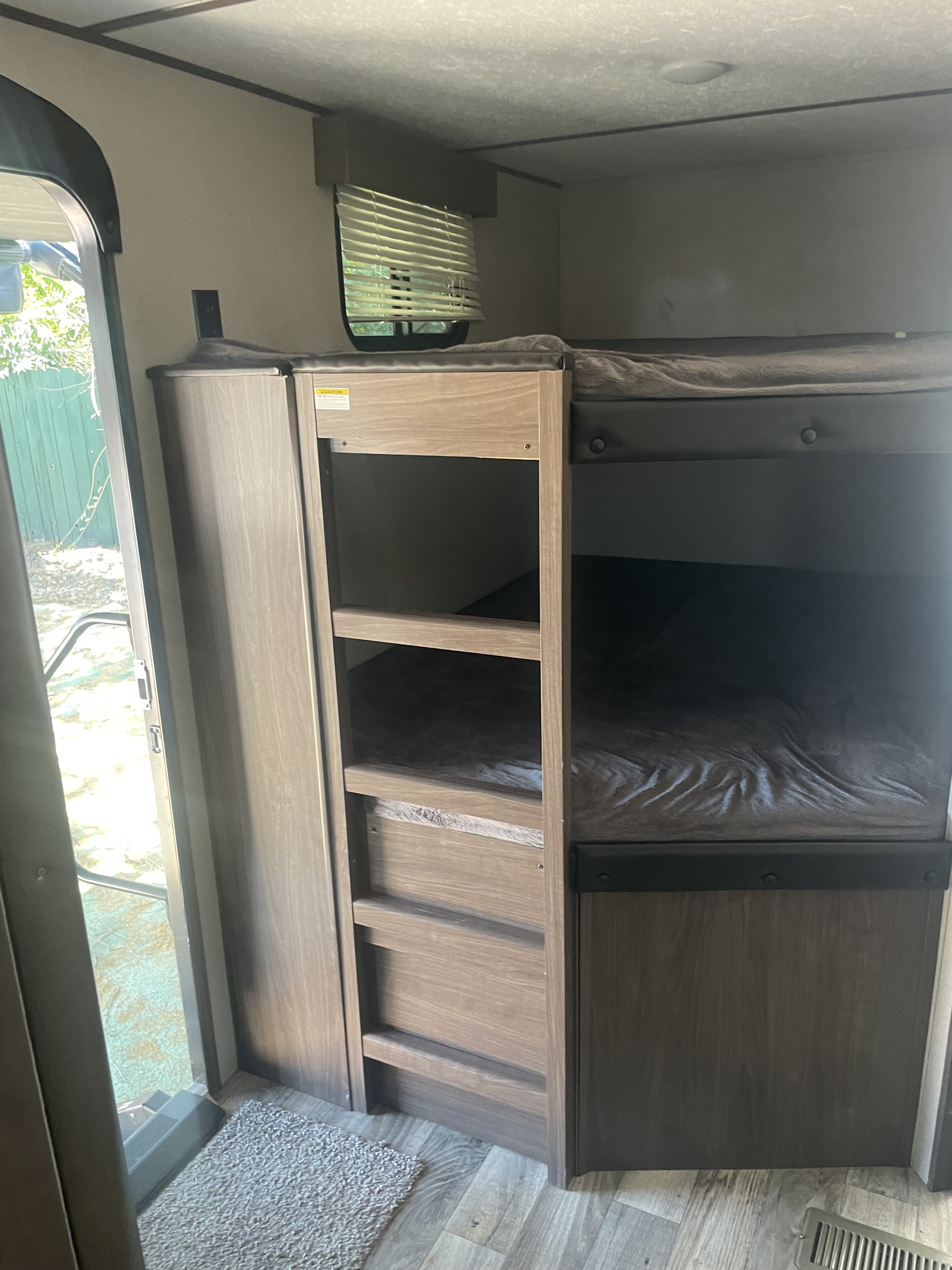 Inside an RV rental: bunk beds with a storage cabinet next to the open entry door, featuring wood-look finishes.. Keystone RV Hideout LHS 2019