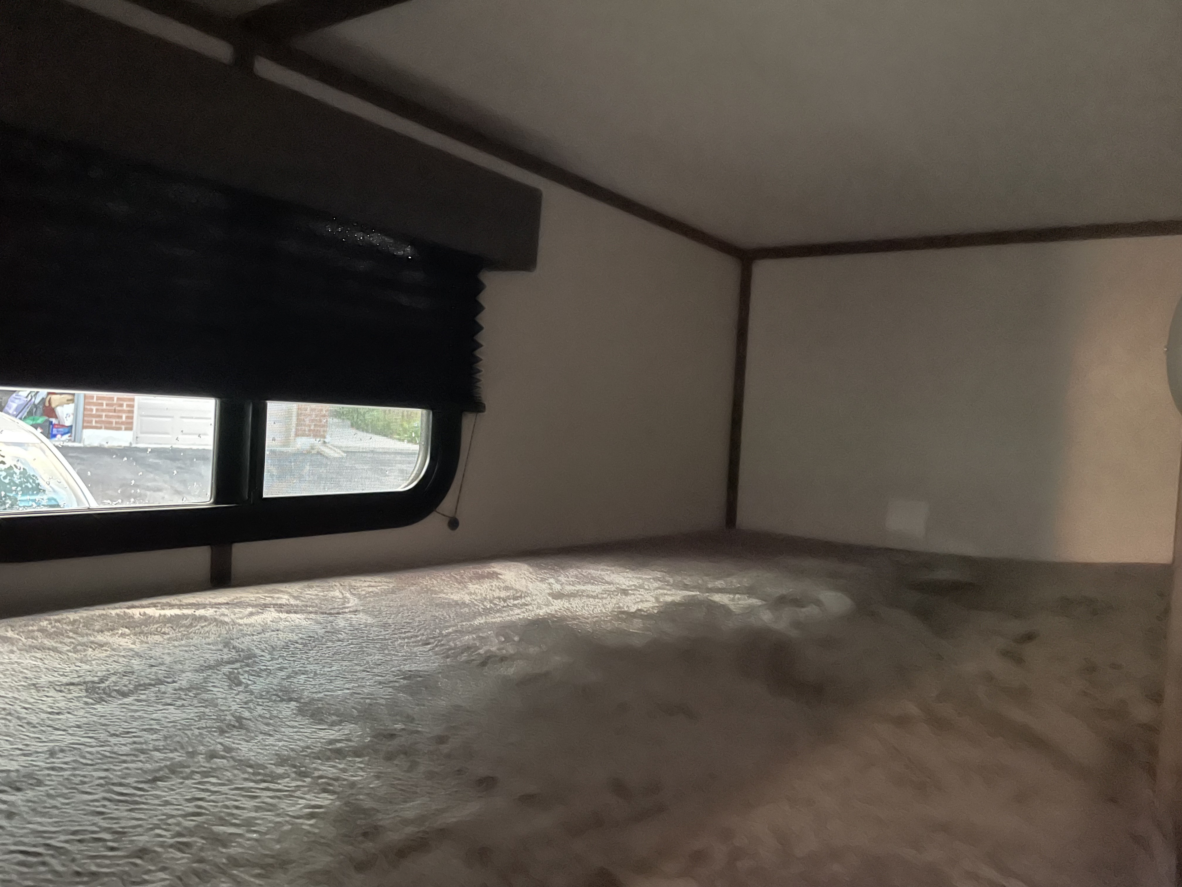 RV rental bunk bed. Compact interior with a window view of a garage and car. Dark blind partially down.. Riverside Retro 190bh 2023