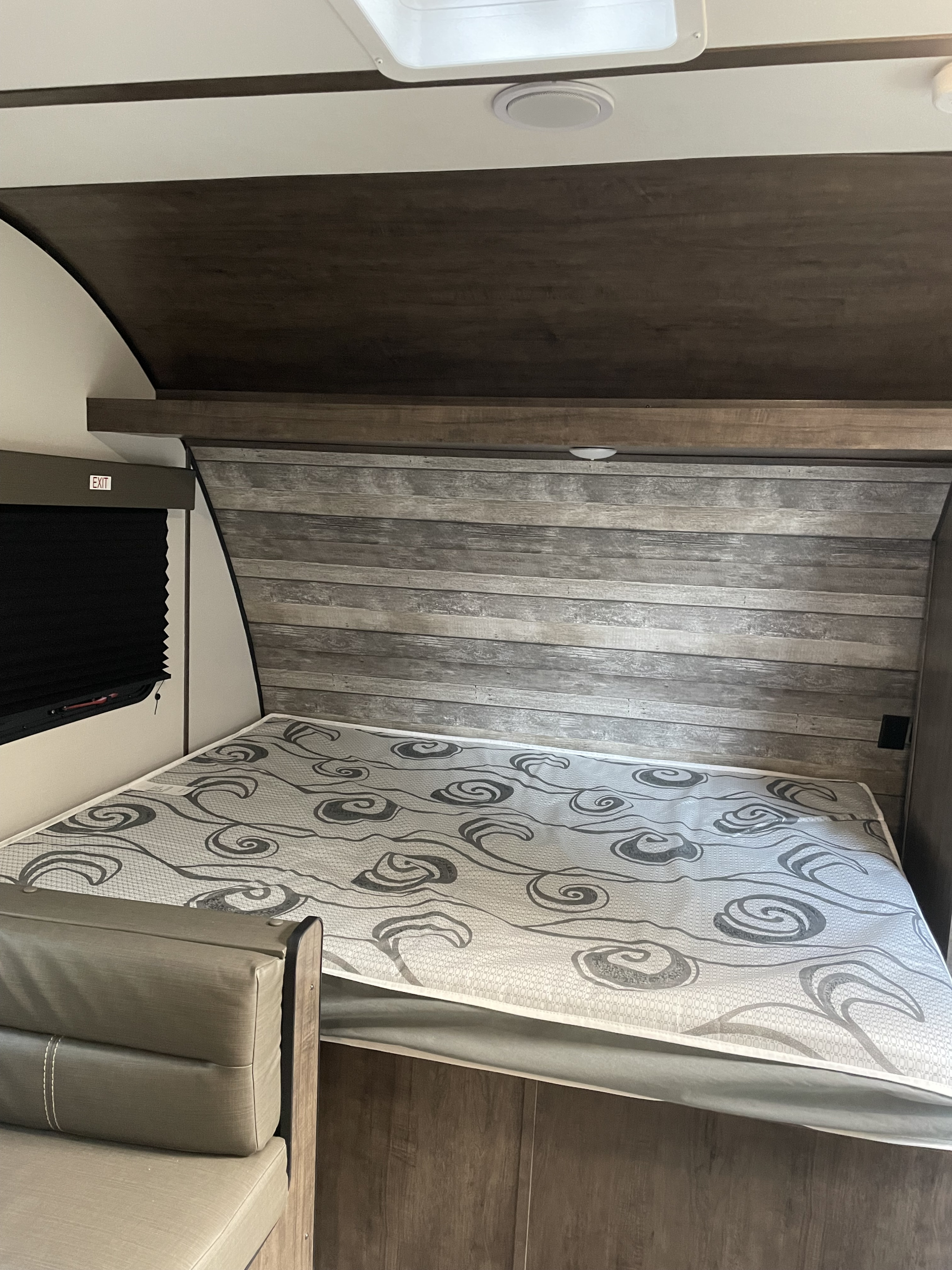 RV rental interior showcasing a bed with a patterned mattress, wood-look headboard, and a window with an exit sign.. Riverside Retro 190bh 2023