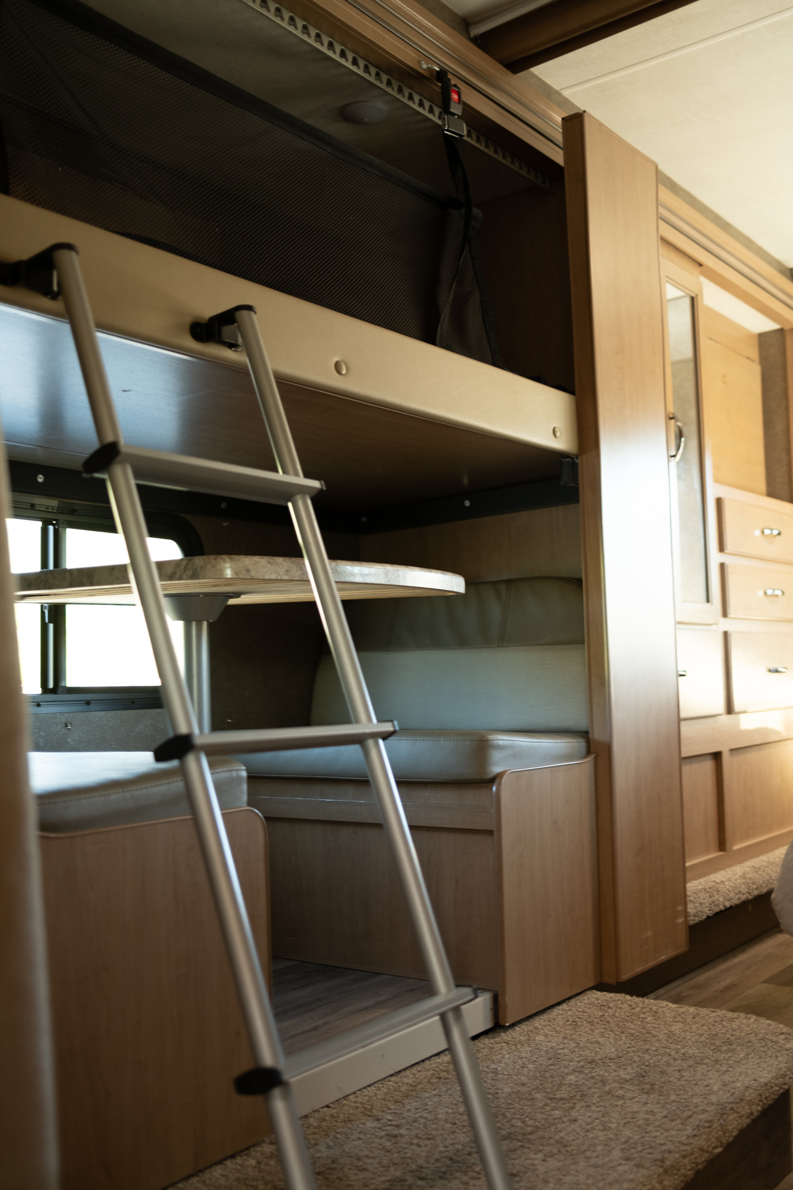 RV rental's family-friendly interior: a bunk bed with safety net and ladder, overlooking a dinette booth for meals.. Thor Four Winds 2021