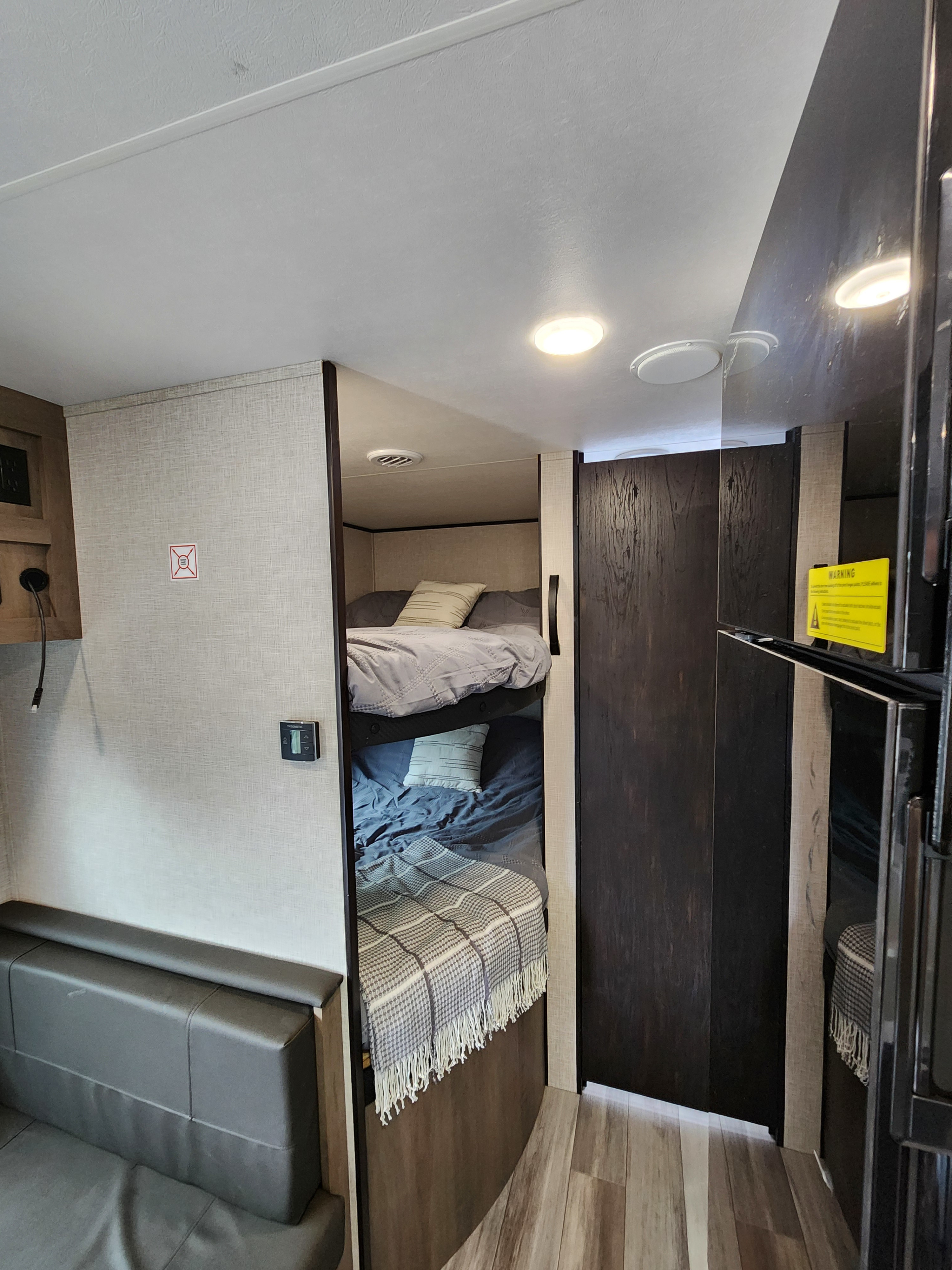 Inside this RV rental, find stacked bunk beds, a plush bench seat, and a large refrigerator in a bright, functional space.. Jayco Jay Flight 2024