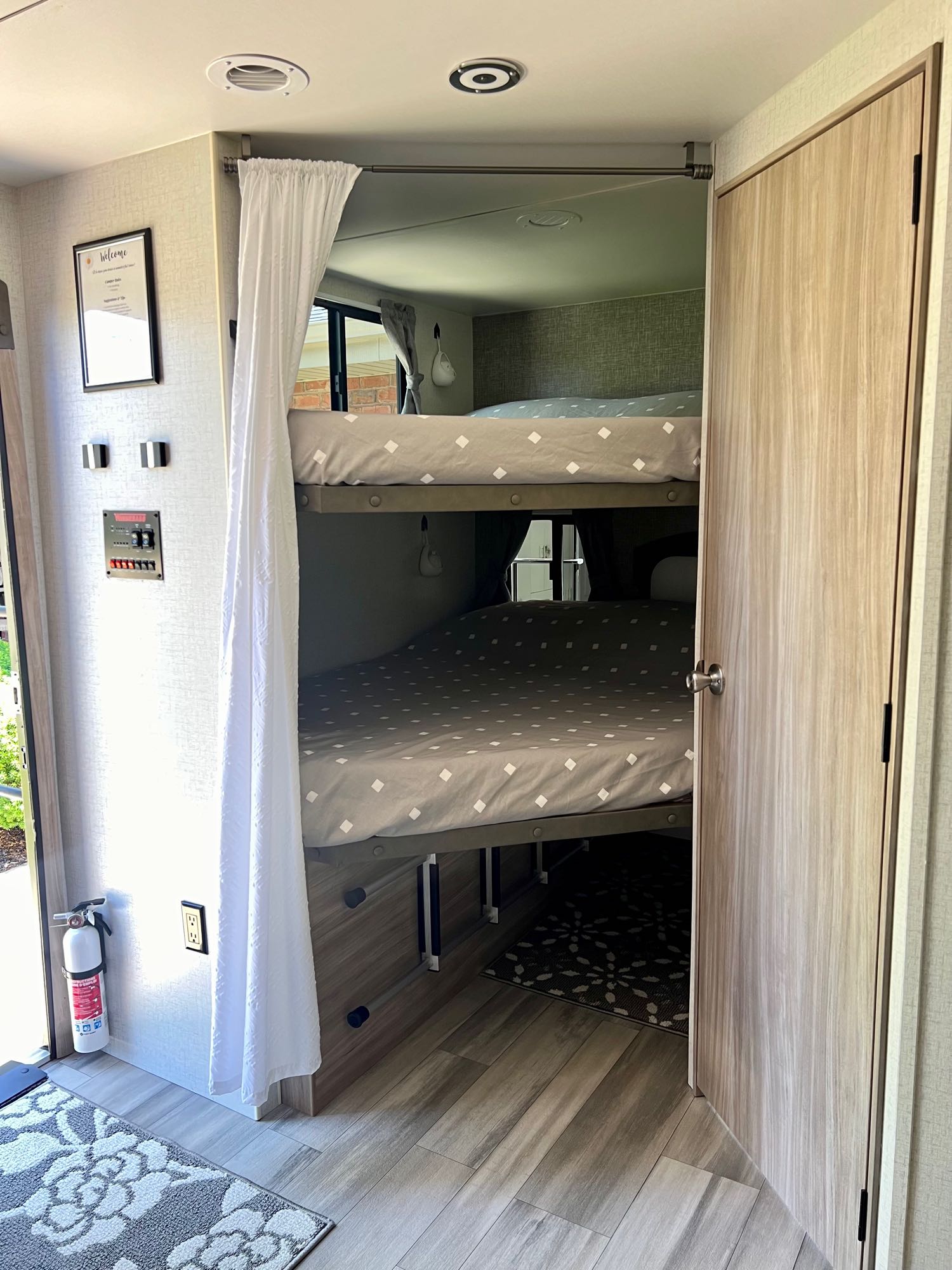 View of an rv rental's cozy interior, showing bunk beds with a privacy curtain, control panel, and fire extinguisher by the door.. Winnebago 2301BHS 2022