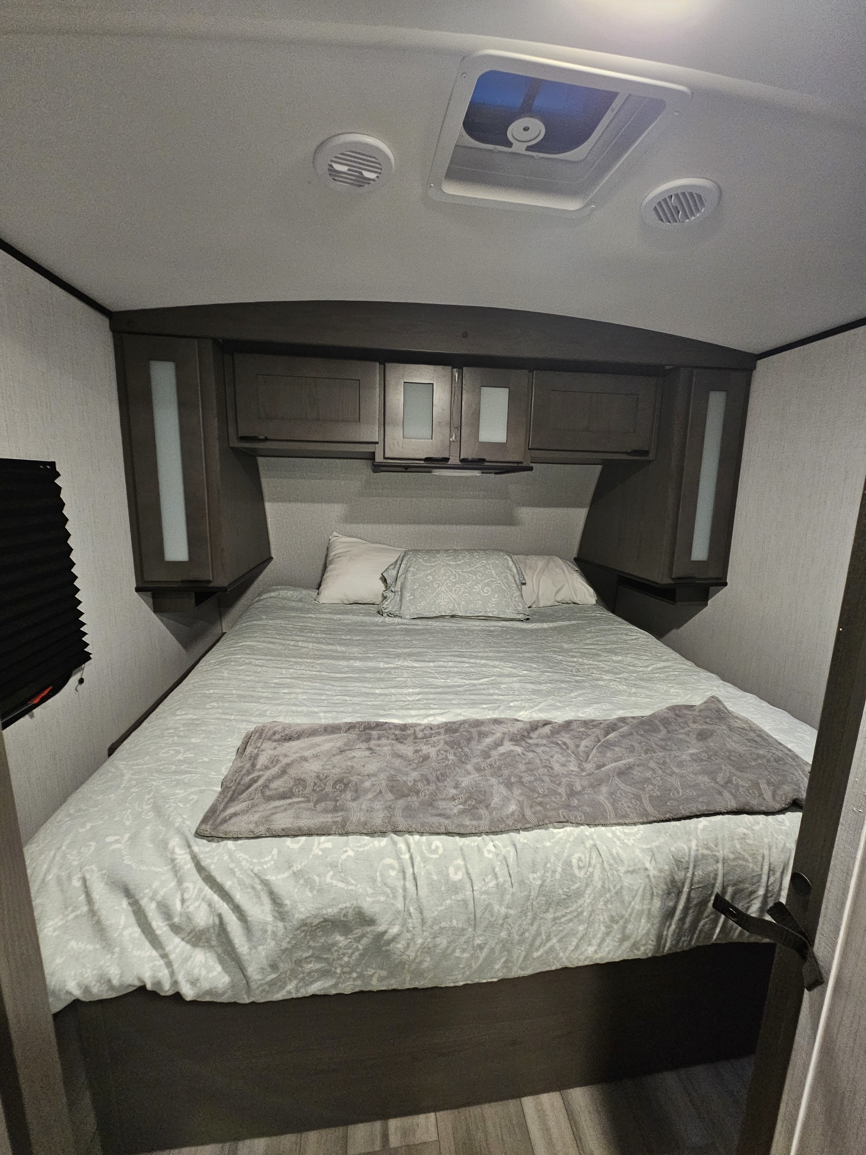 Cozy RV rental bedroom features a comfy bed, dark wood overhead cabinets, ceiling vents, and a skylight for natural light.. Cruiser RV MPG 2840BH 2023