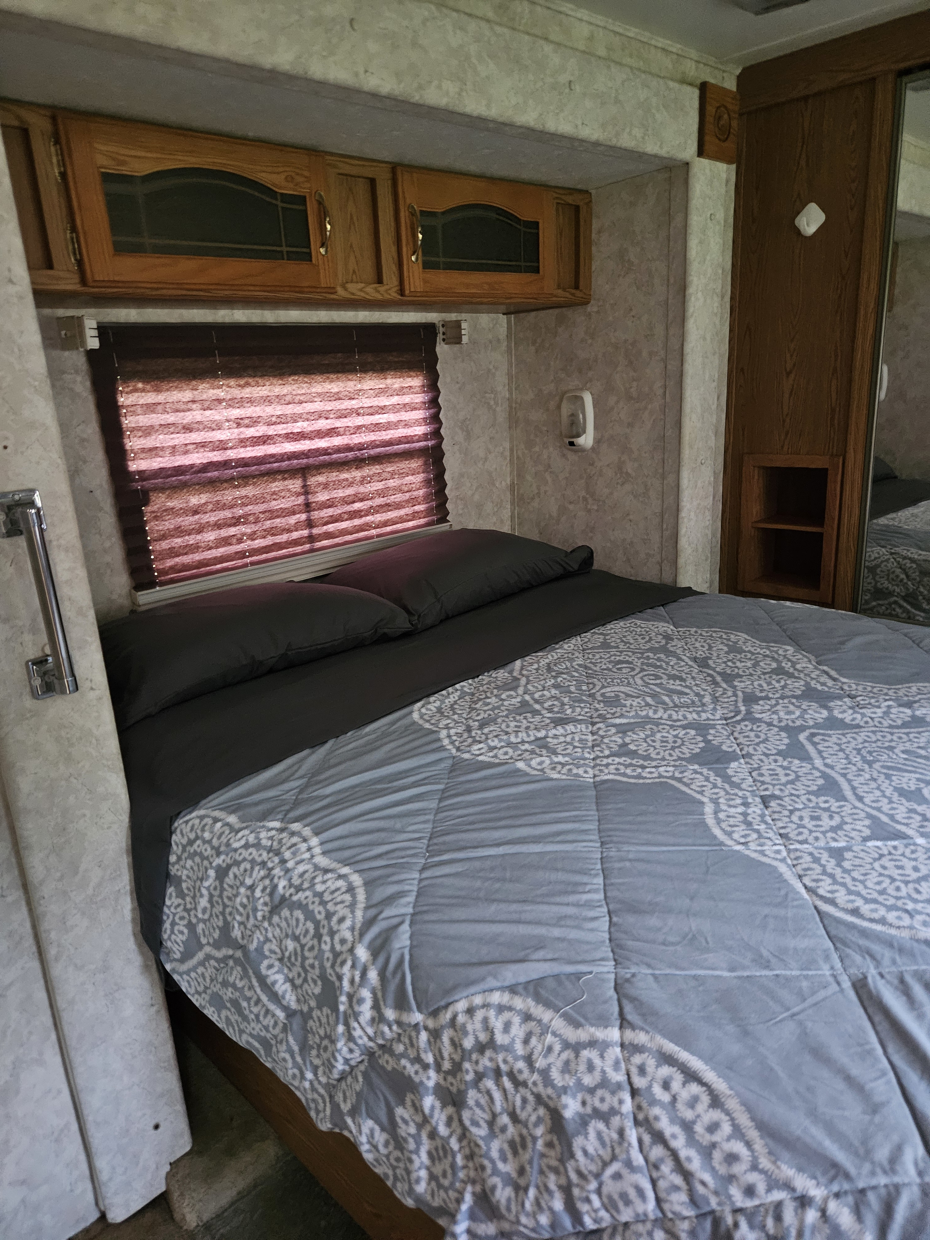Cozy RV rental bedroom with a blue patterned comforter, dark bedding, wood overhead cabinets, and window blinds.. Keystone RV Big Sky Montana 2003