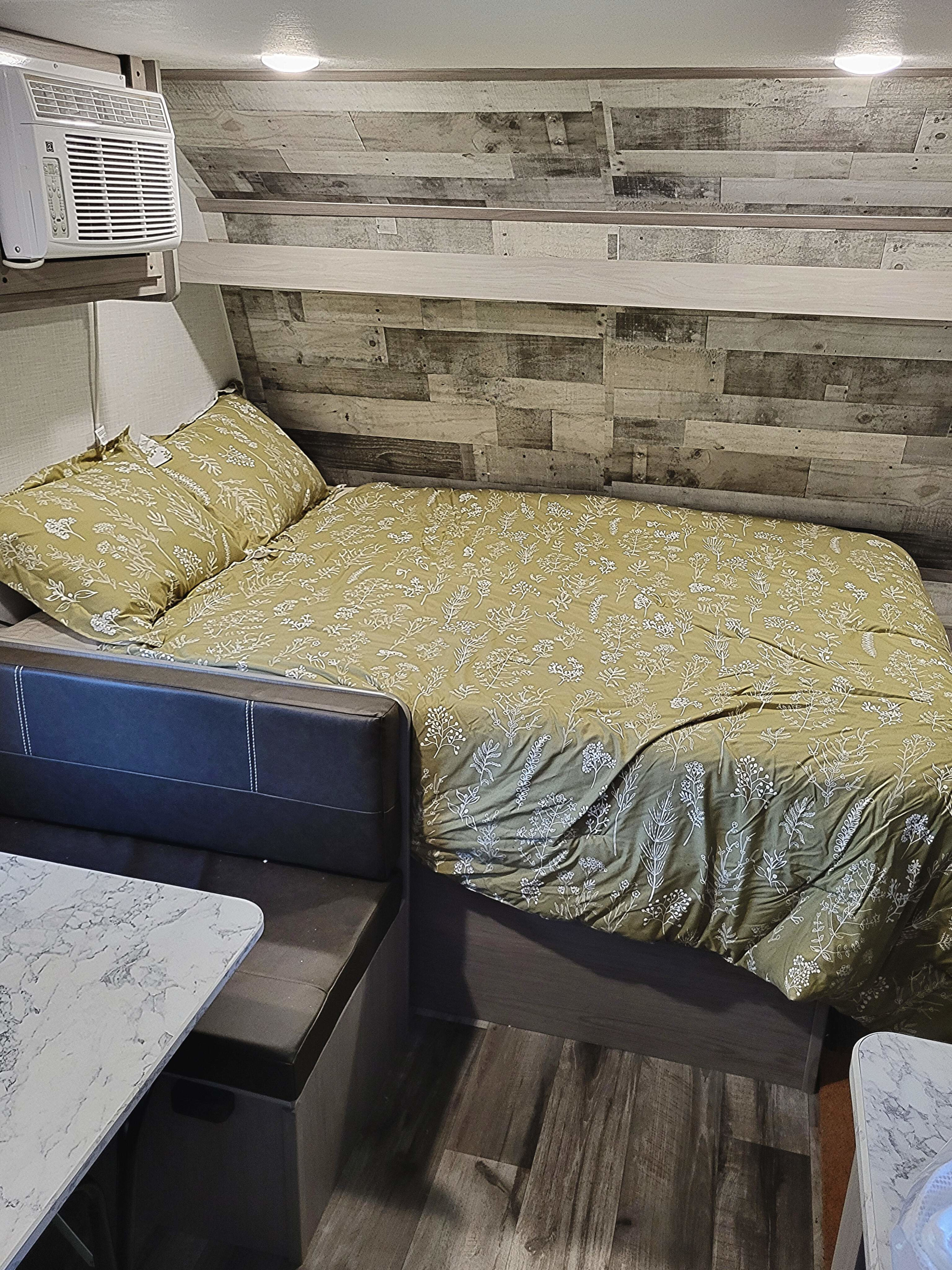 RV rental interior featuring a cozy bedroom area with green floral bedding, mounted AC unit, wood paneling, and dinette.. Dutchmen Coleman Lantern LT 2023