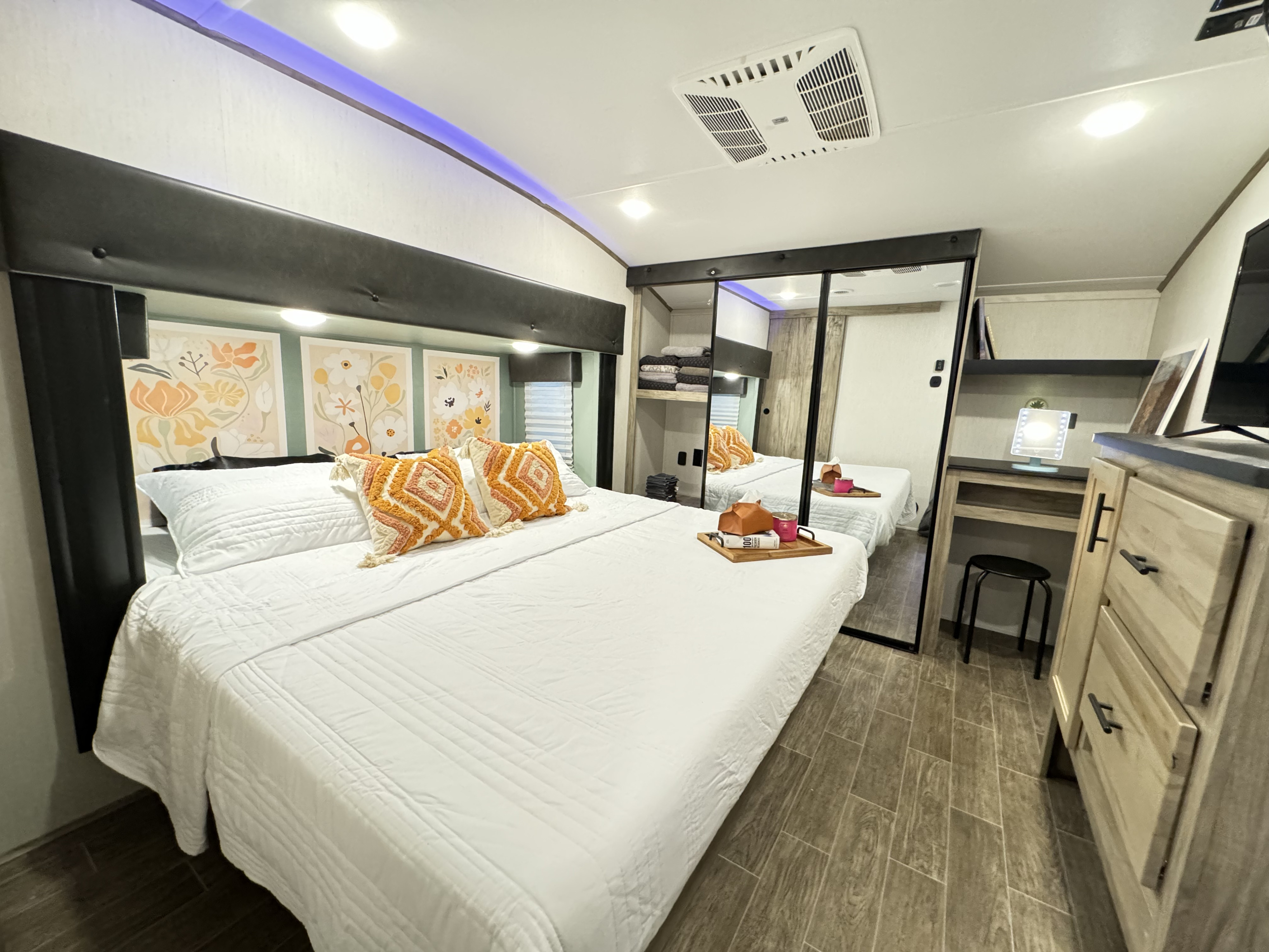 Stylish RV rental bedroom: comfy bed, floral art, mirrored closet, and vanity. Enjoy a modern mobile living space.. Forest River Cherokee Arctic Wolf 2022