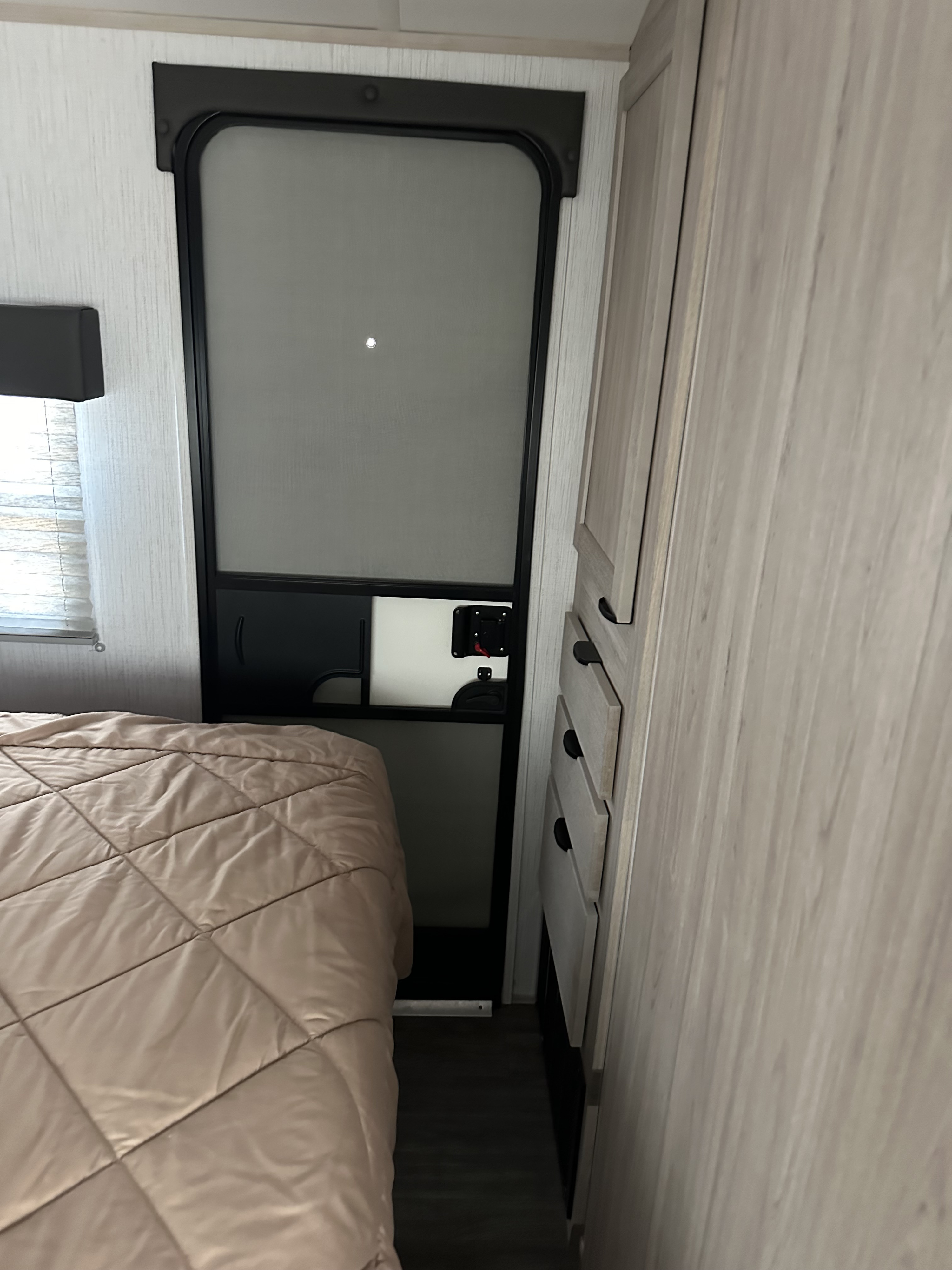 Cozy RV rental bedroom featuring a quilted bedspread, interior door, and light wood-grain cabinet storage.. EarthCruiser 248RKS 2022