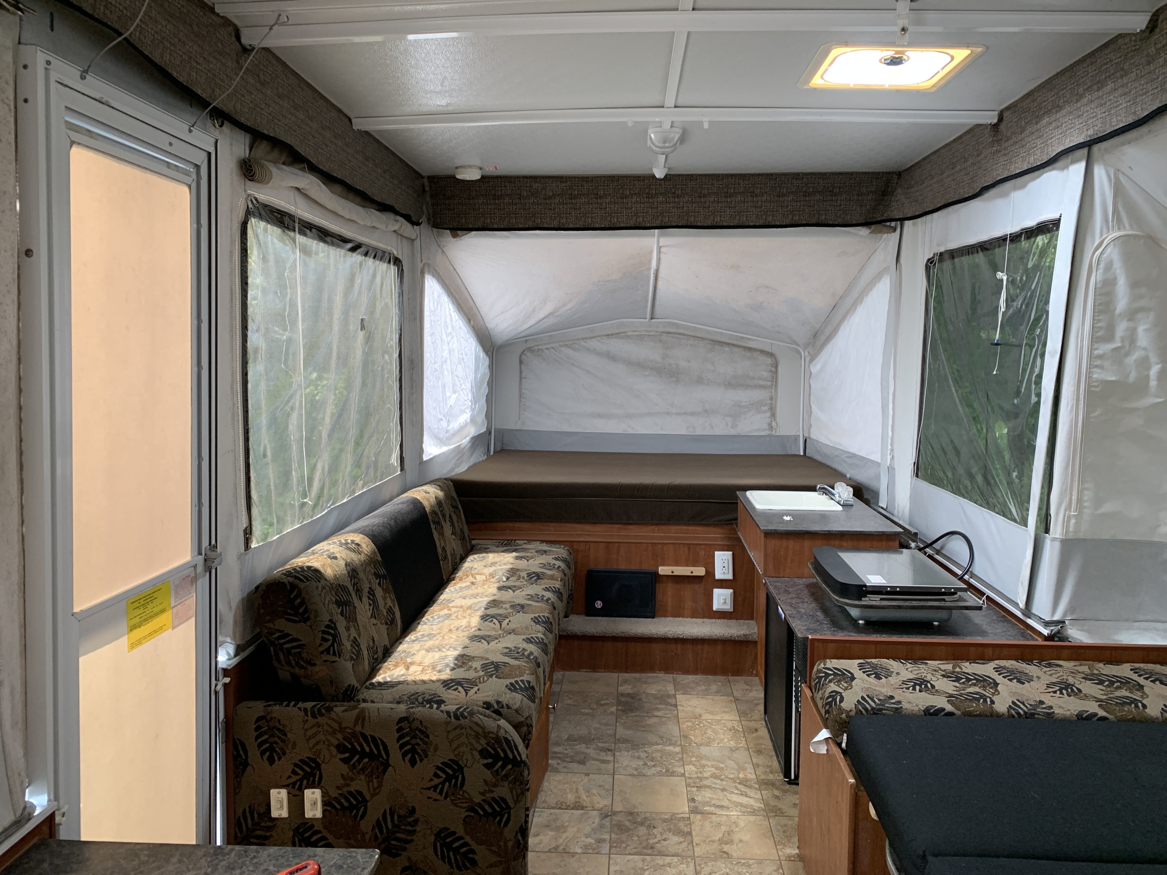 Inside a pop-up RV rental: cozy interior with a couch, bed, kitchen, and ample windows for your next adventure.. Jayco Jay 2012