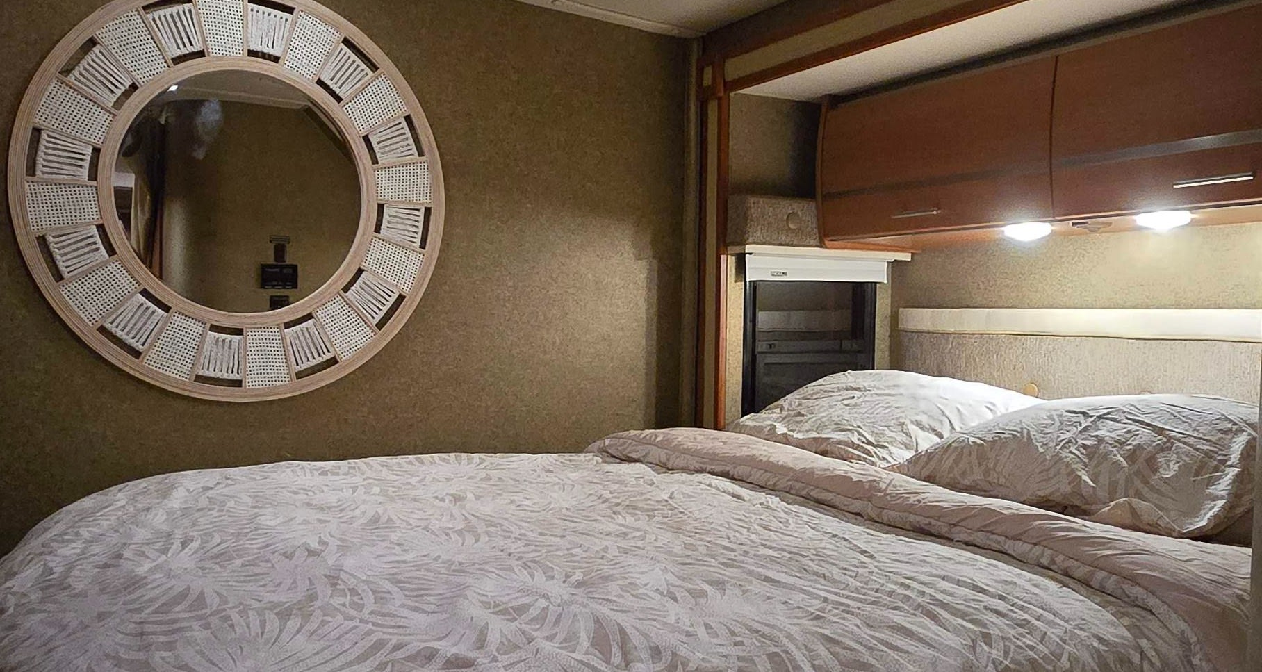 Spacious RV rental bedroom featuring a comfy bed, round decorative mirror, and overhead cabinets for a cozy trip.. Winnebago Via 2013