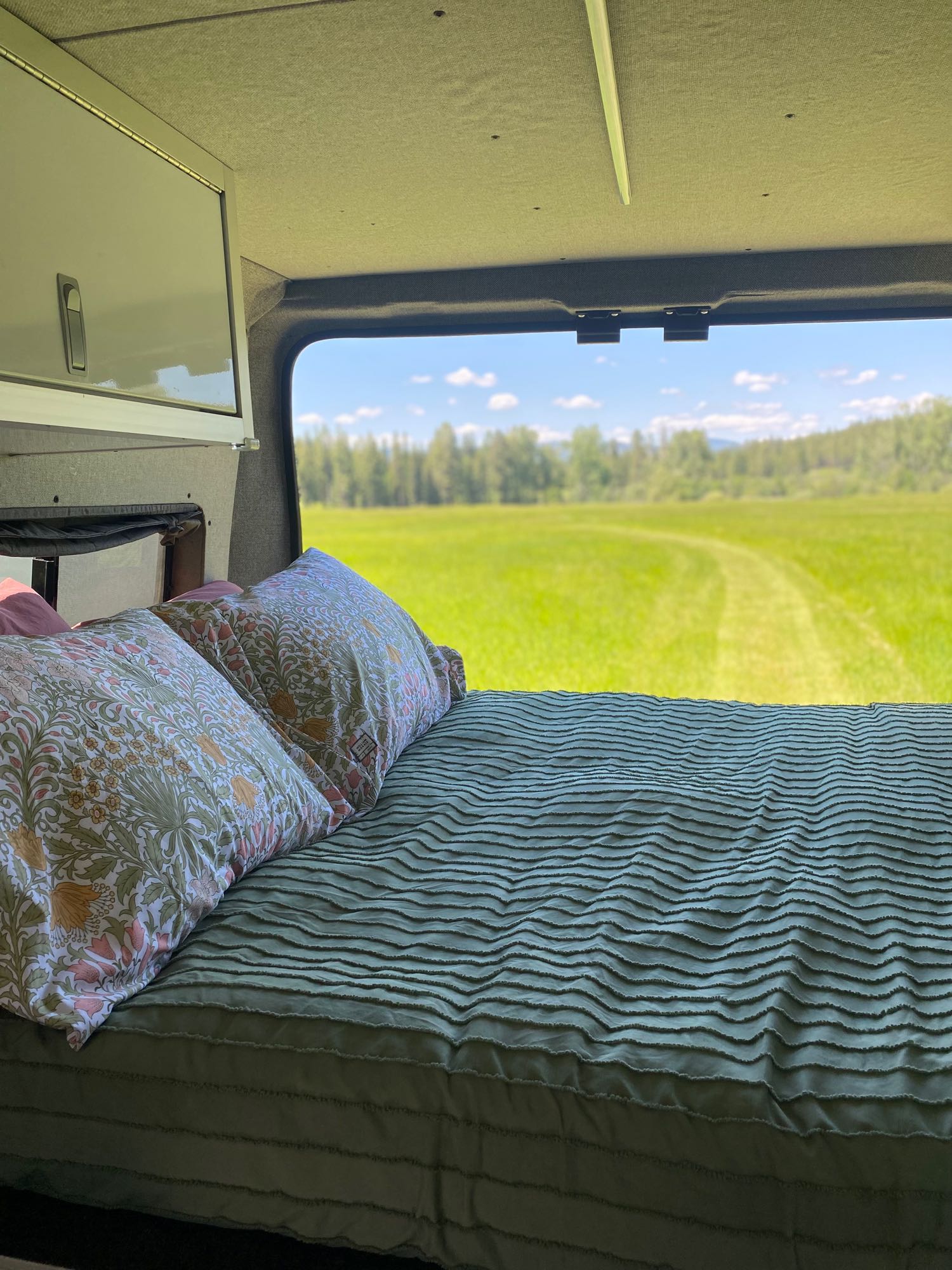 RV rental: interior bed with floral pillows, offering a window view of a vast, bright green field.. Dodge Ram 1500 2017