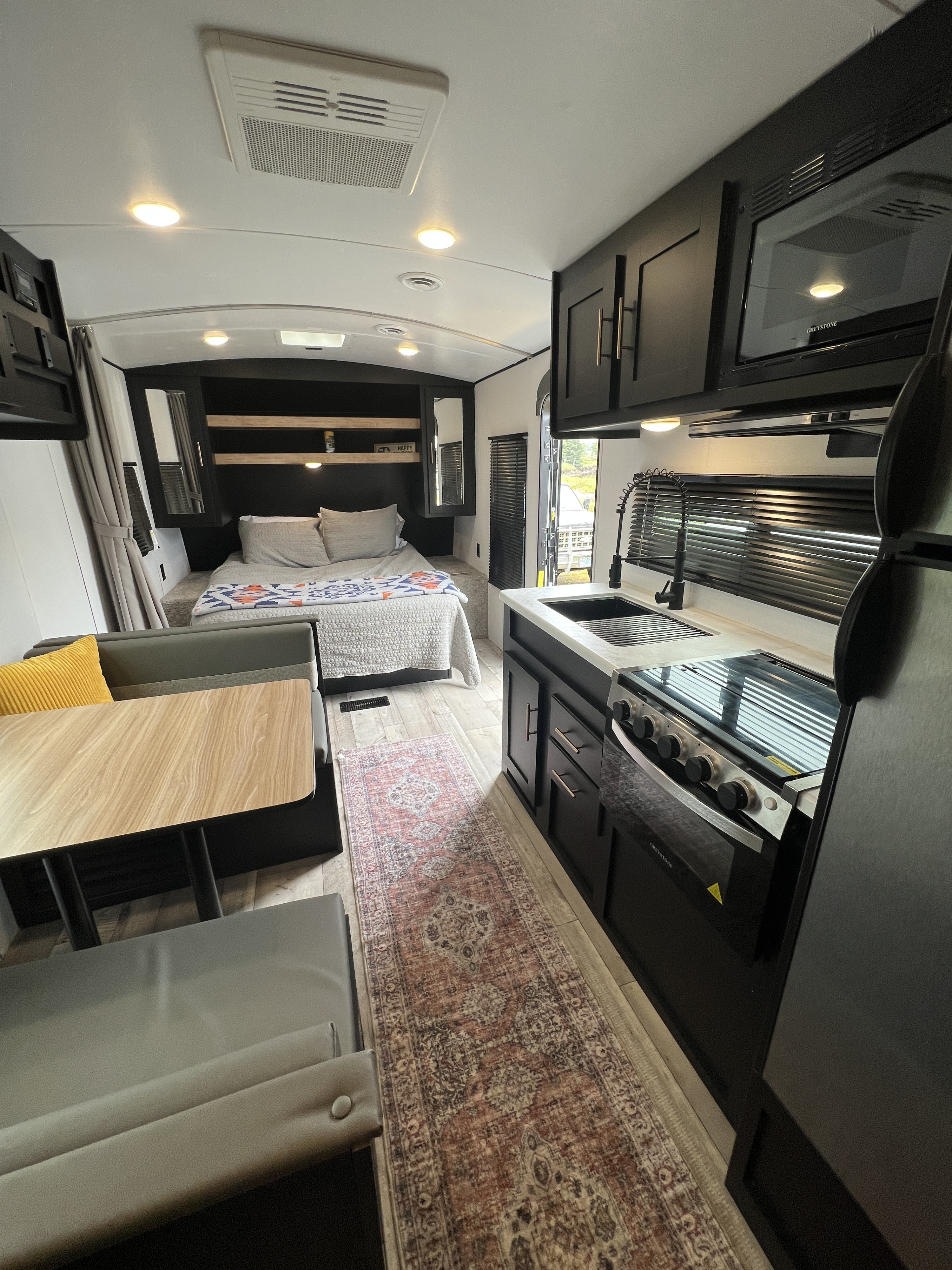 Spacious rv rental interior featuring a bed, dining booth, and full kitchen with black appliances and cabinets.. Keystone RV Springdale 2022