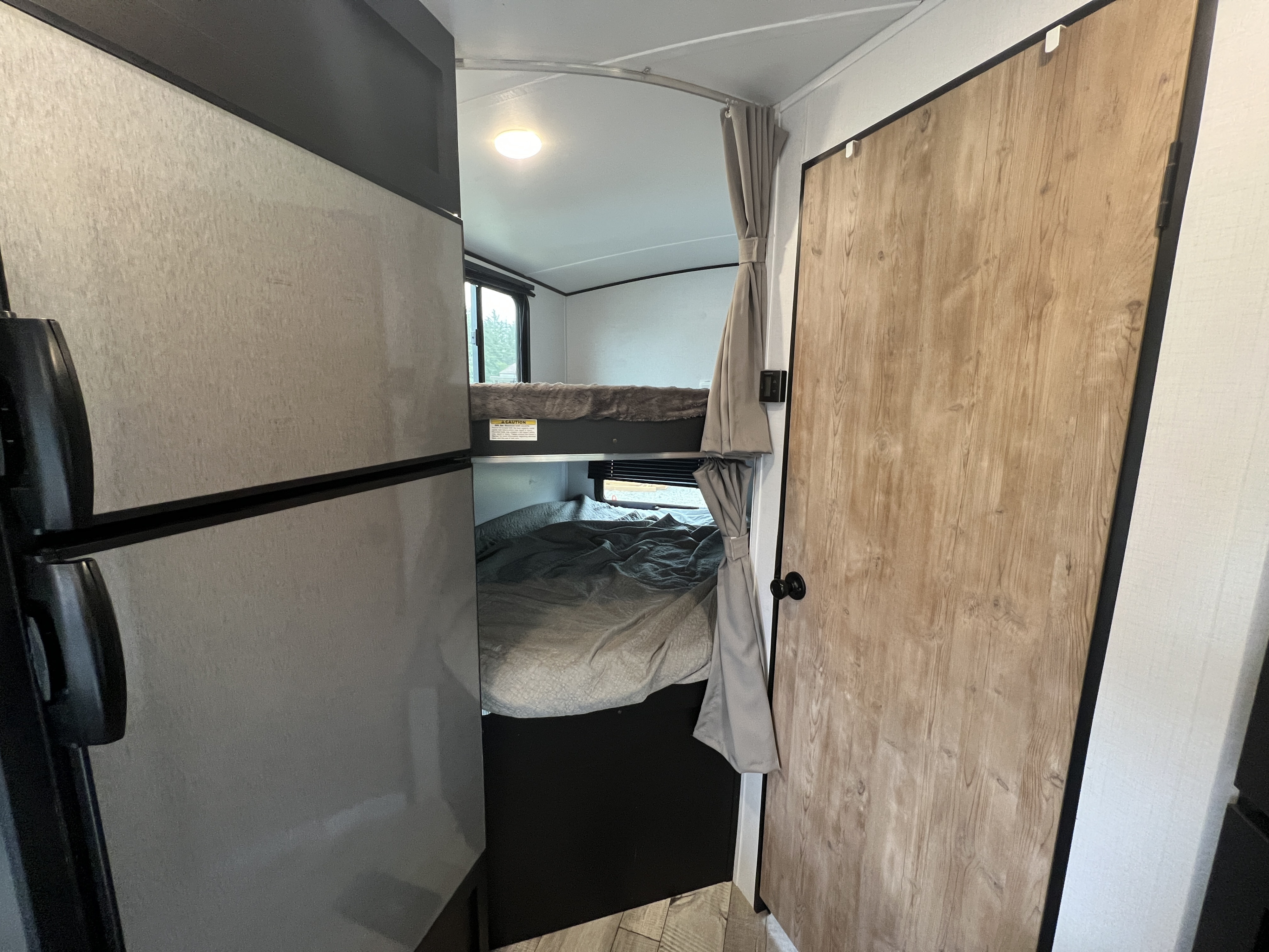 Cozy RV rental interior featuring a fridge, bunk beds with curtains, and a wooden door. Perfect for family trips!. Keystone RV Springdale 2022