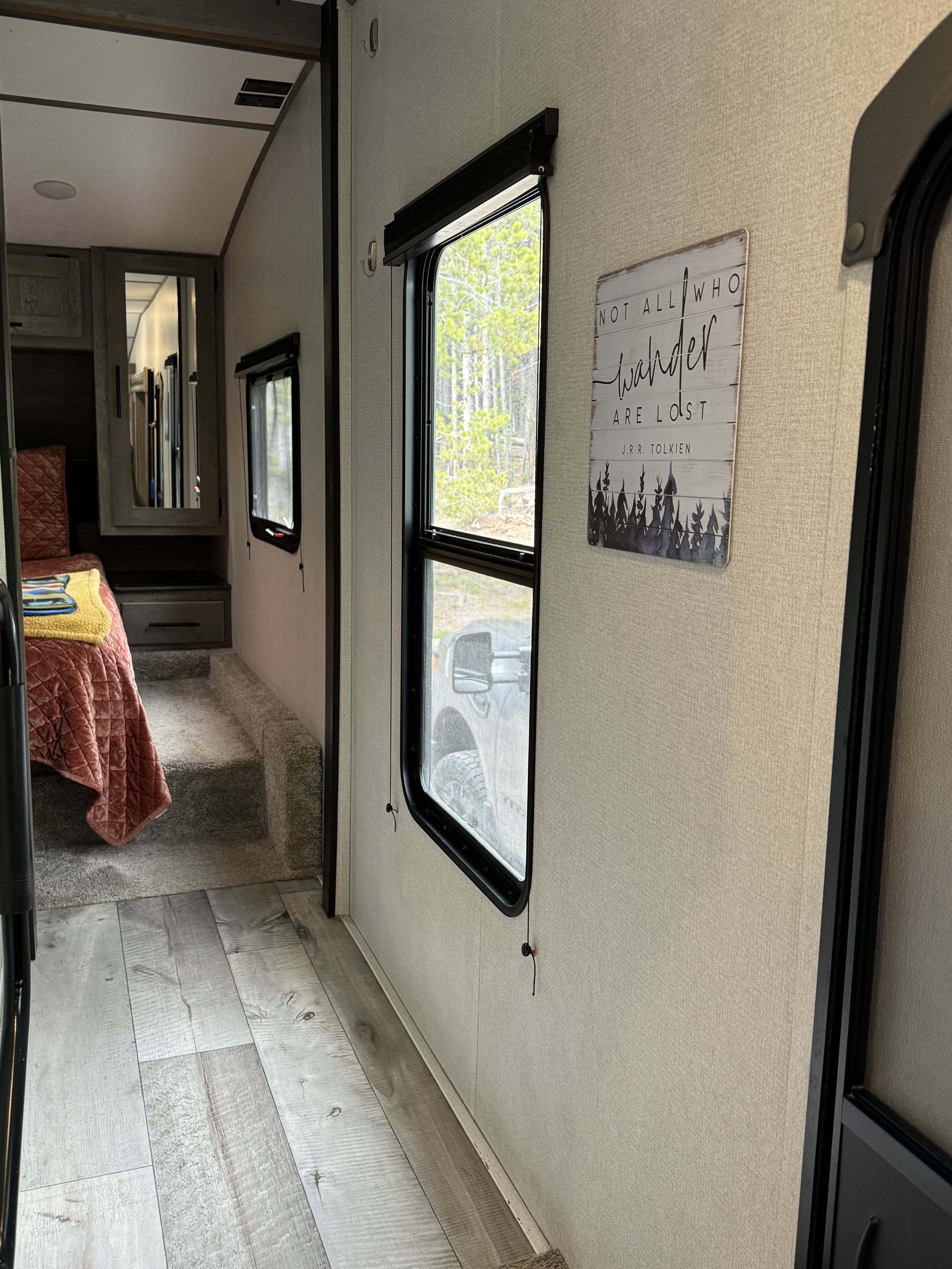 RV rental interior features an elevated bedroom, modern wood-look floors, and large windows revealing an outdoor scene.. Keystone Springdale 2021