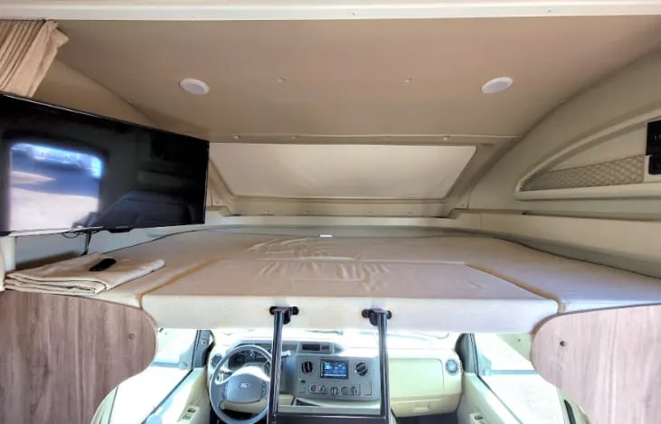 RV rental interior: A spacious over-cab bunk bed with a mounted TV, seen above the dashboard.. Entegra Coach Odyssey 2019